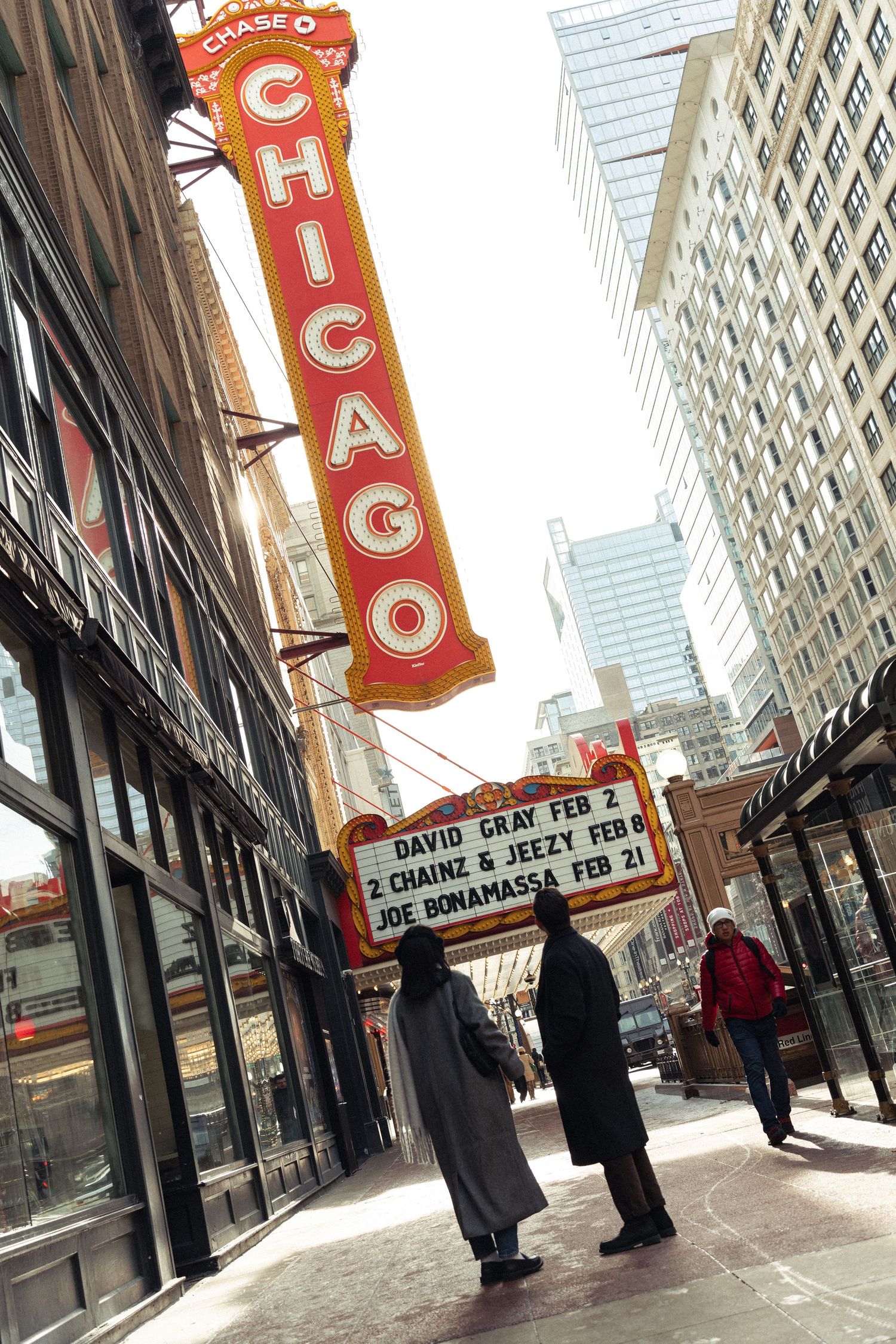 People walk beneath the iconic red Chicago Theatre sign on State Street in downtown Chicago on a winter day.