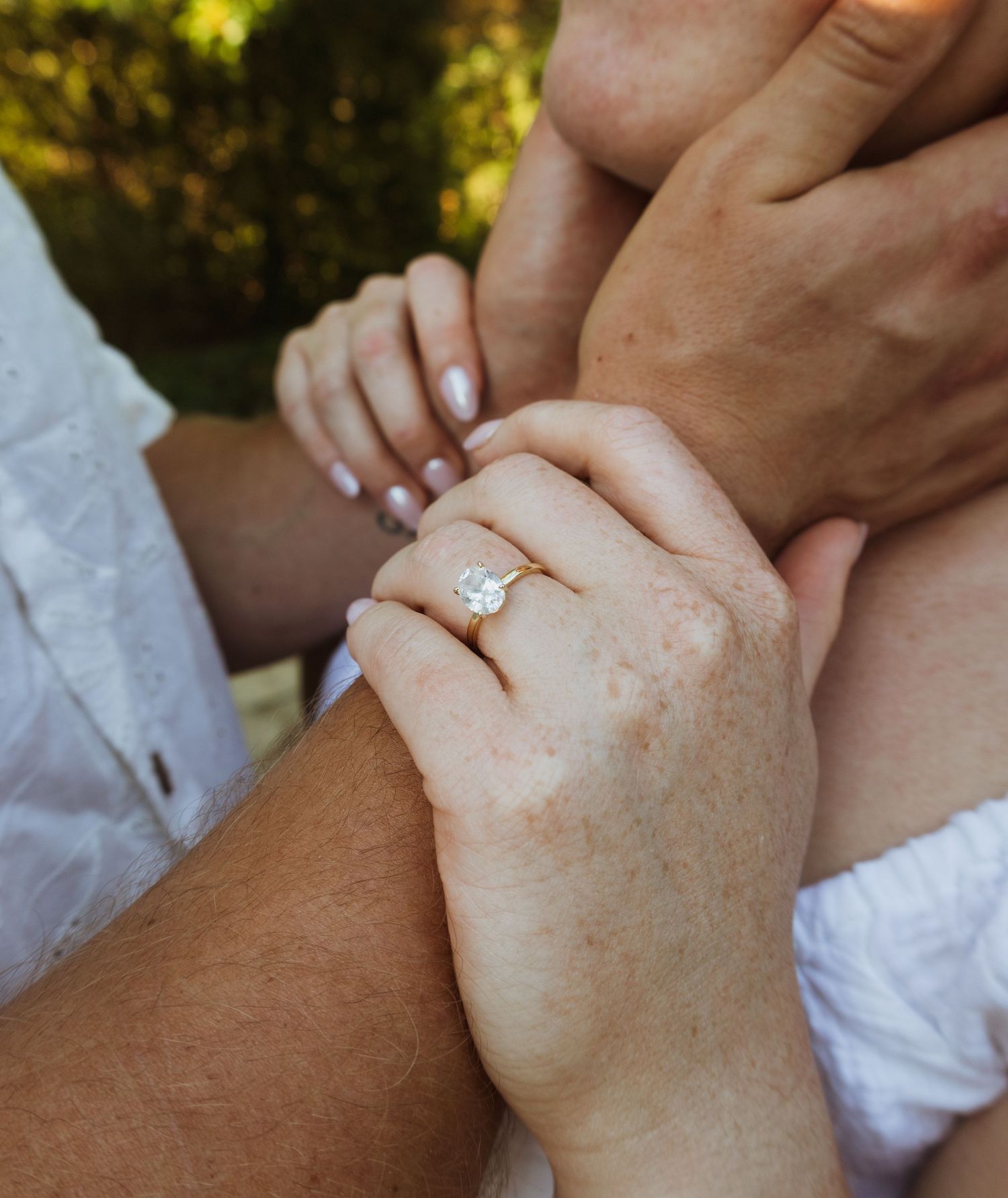 Close-up of hands holding with a stunning oval diamond engagement ring on a gold band outdoors.