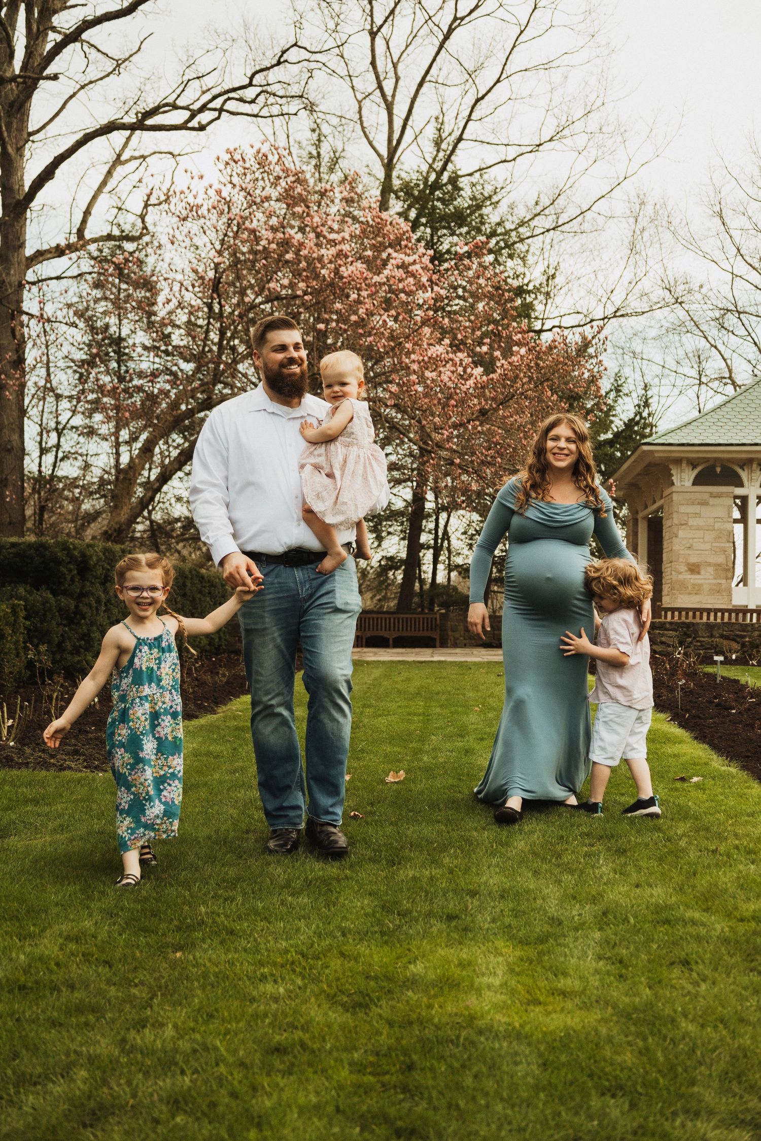 Family enjoying a spring day outdoors with blooming cherry trees and a stone gazebo behind them.
