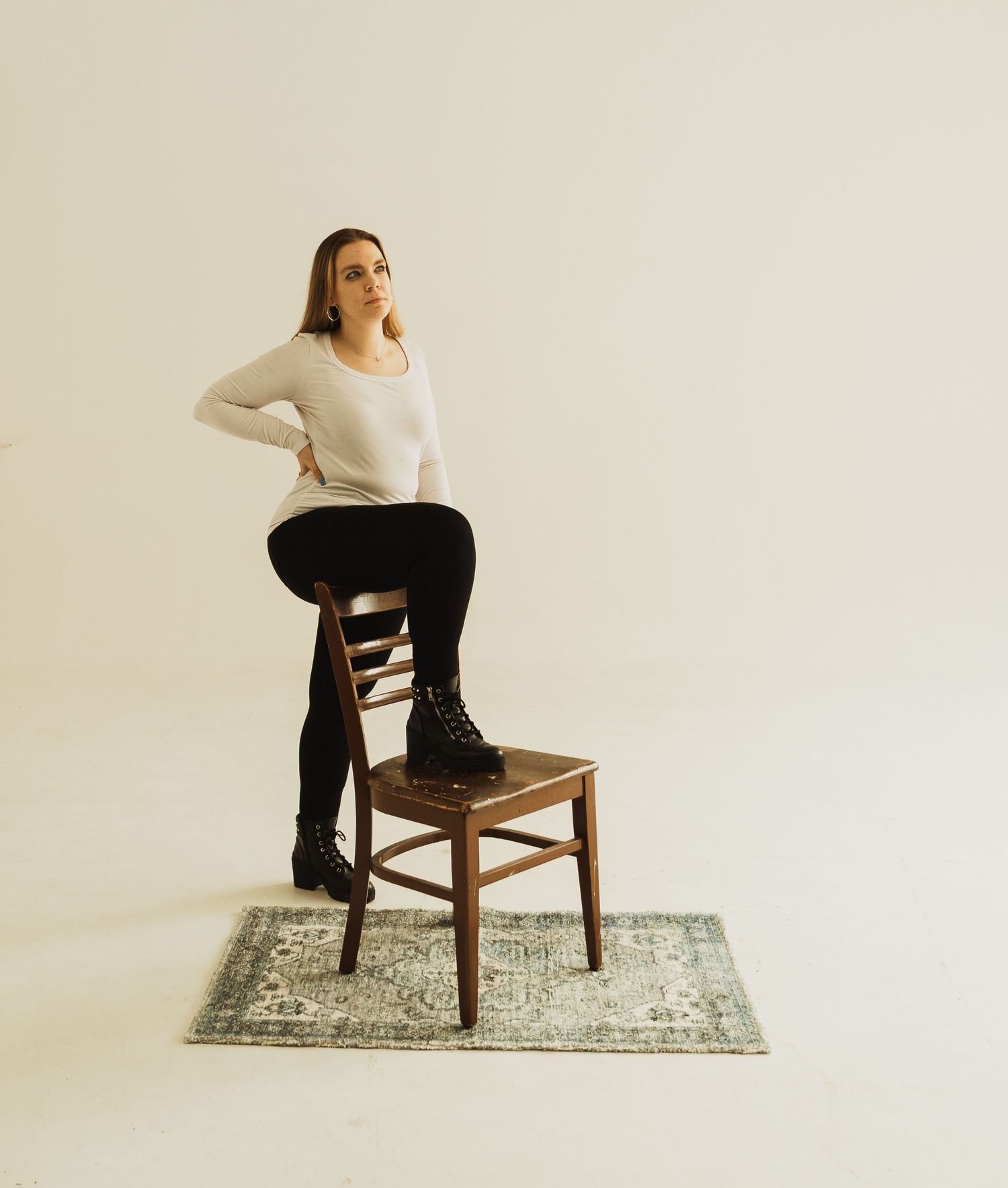 Artistic studio shot with person standing on wooden chair against white backdrop.