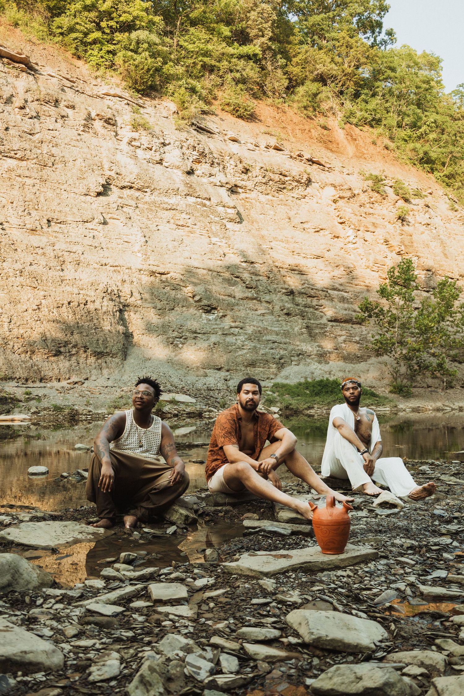Group relaxing on rocky shore beside quarry lake with steep cliffs in the background.