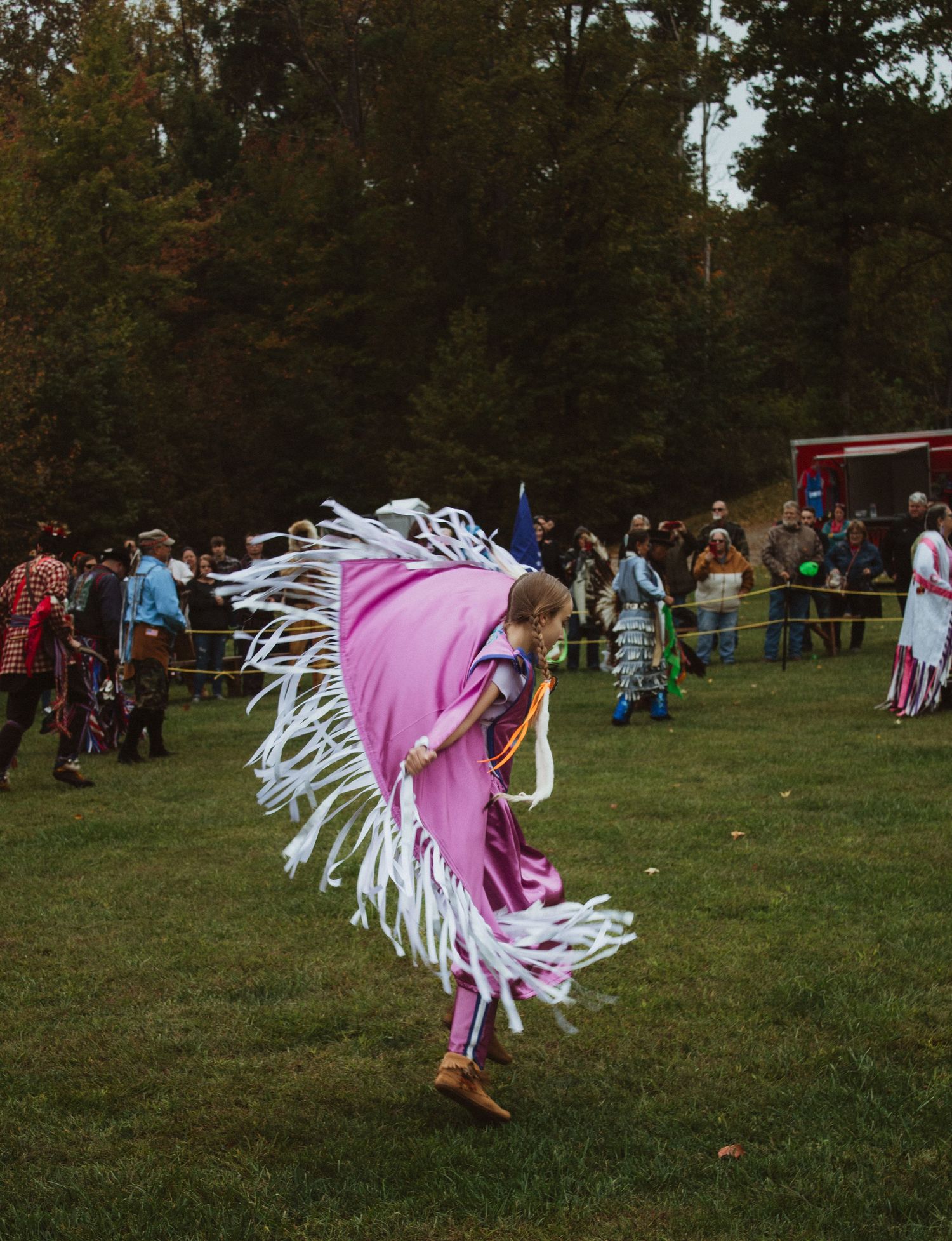 A dancer in pink regalia spins during a traditional performance on a grassy field.