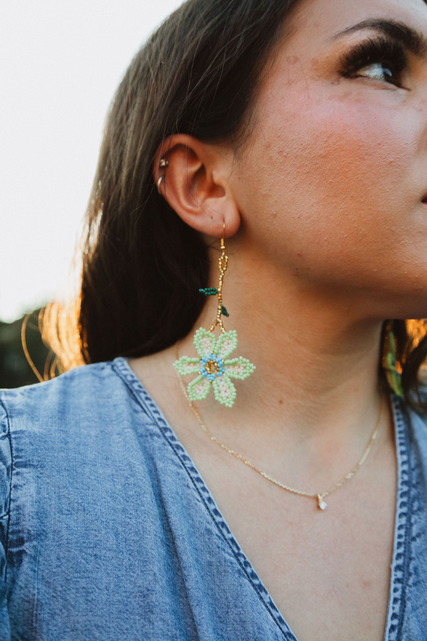 Close-up shots of mint green bow earrings and delicate gold necklace jewelry worn against a denim background.