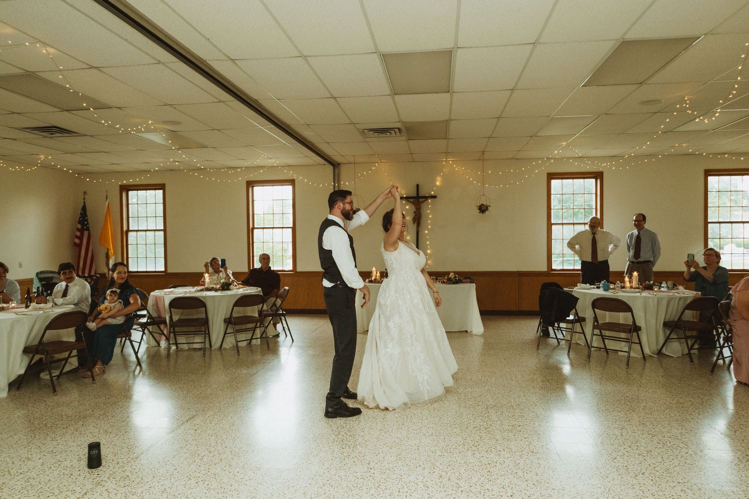 Panoramic view of a reception hall with string lights and windows showing multiple dance moments during a celebration.