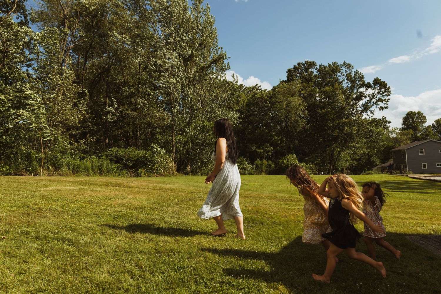 Children playing and running on a sunny green lawn surrounded by trees on a beautiful summer day.