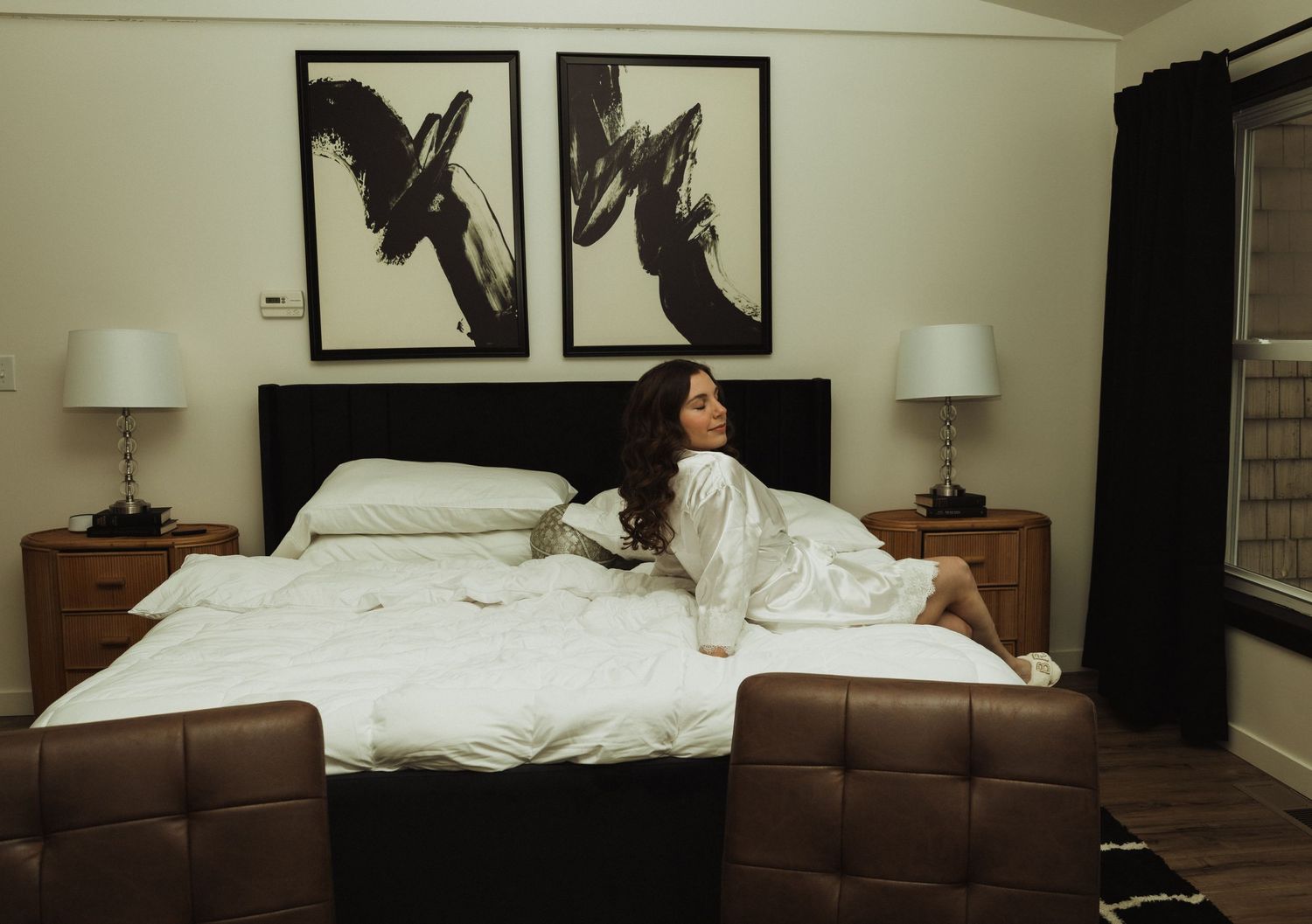 Minimalist bedroom interior featuring abstract black artwork and warm wood furnishings.