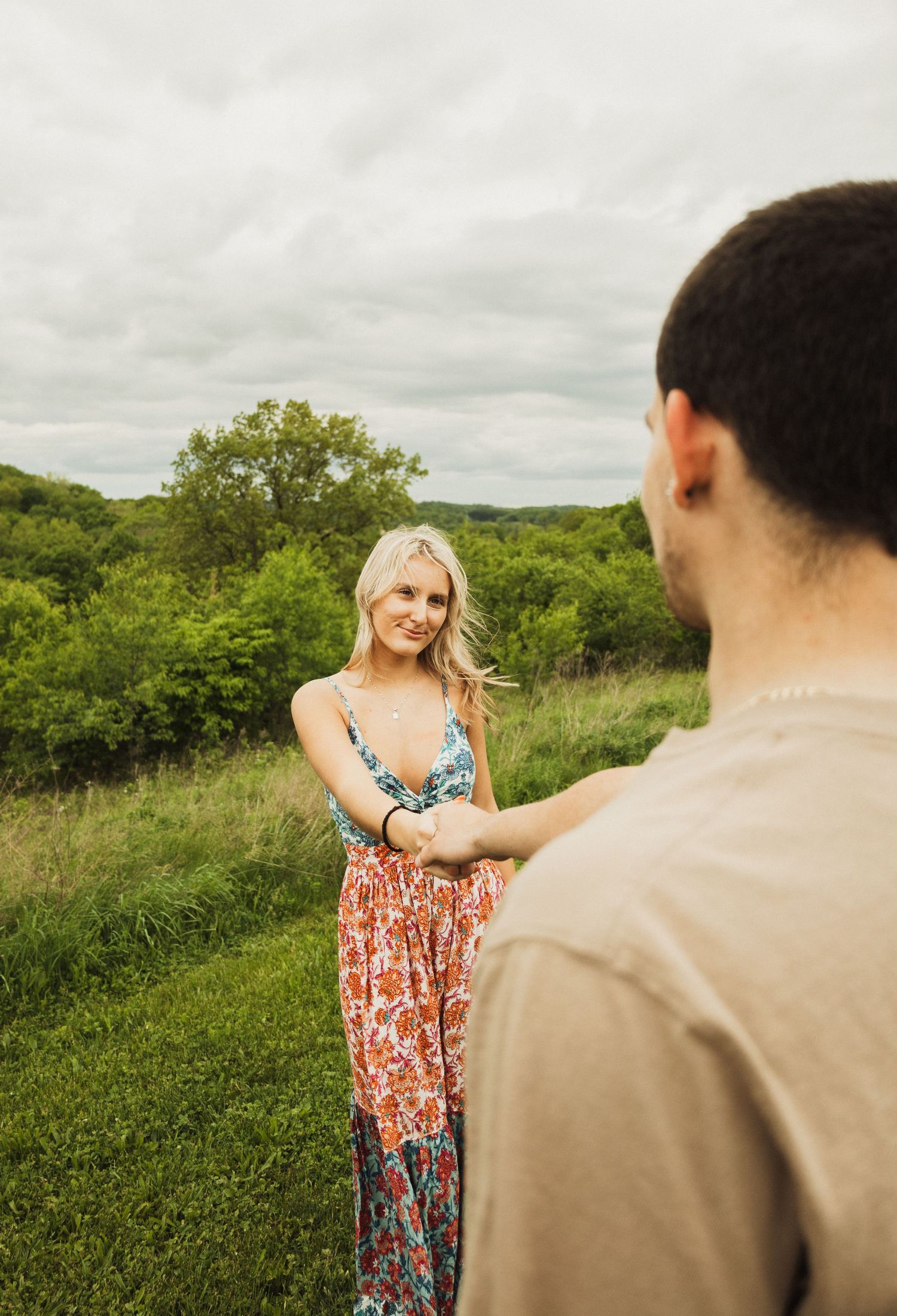 A tender moment between a couple standing in a green meadow with overcast skies.