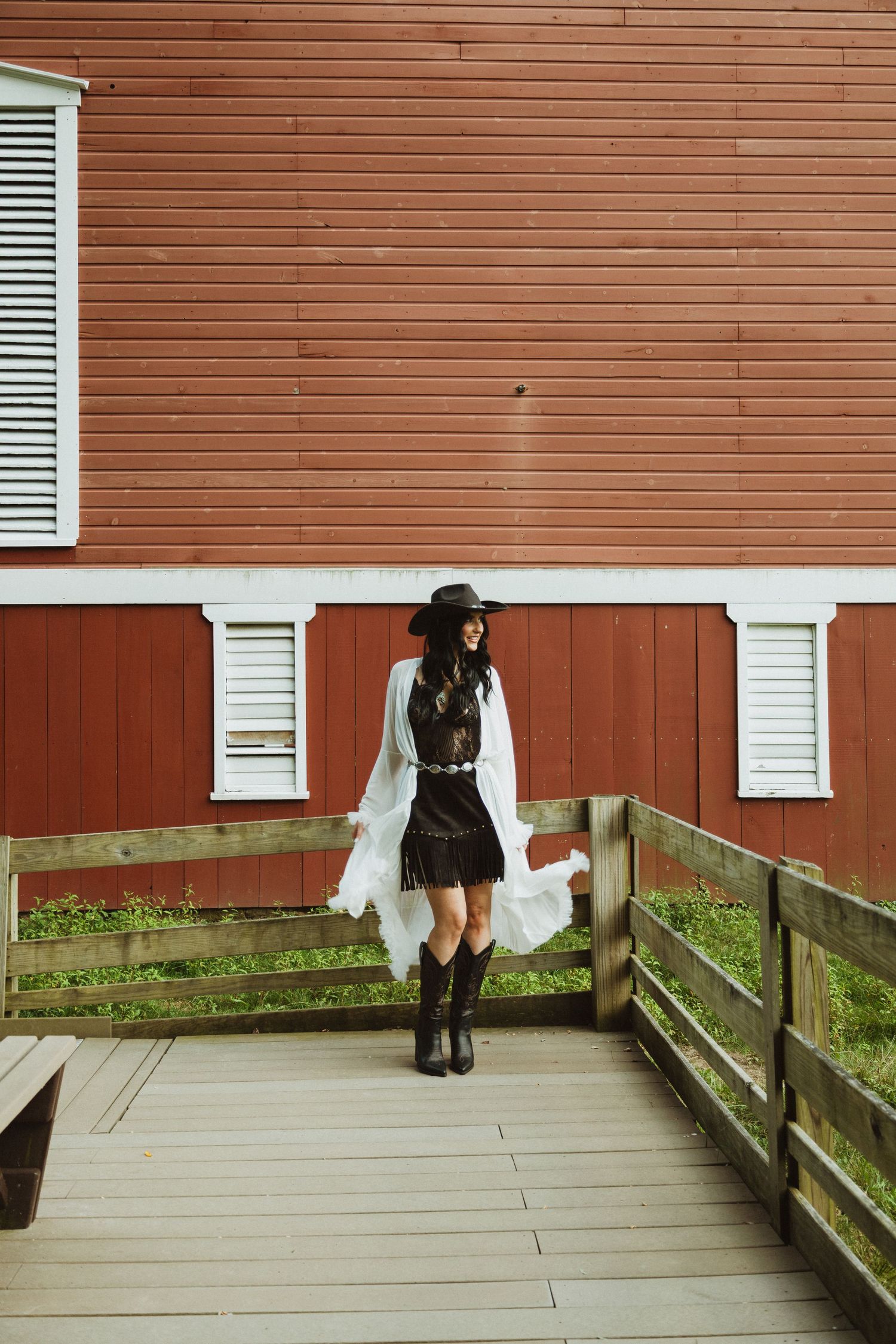 Person in black attire with white shirt and hat walking on a wooden deck next to red barn siding.