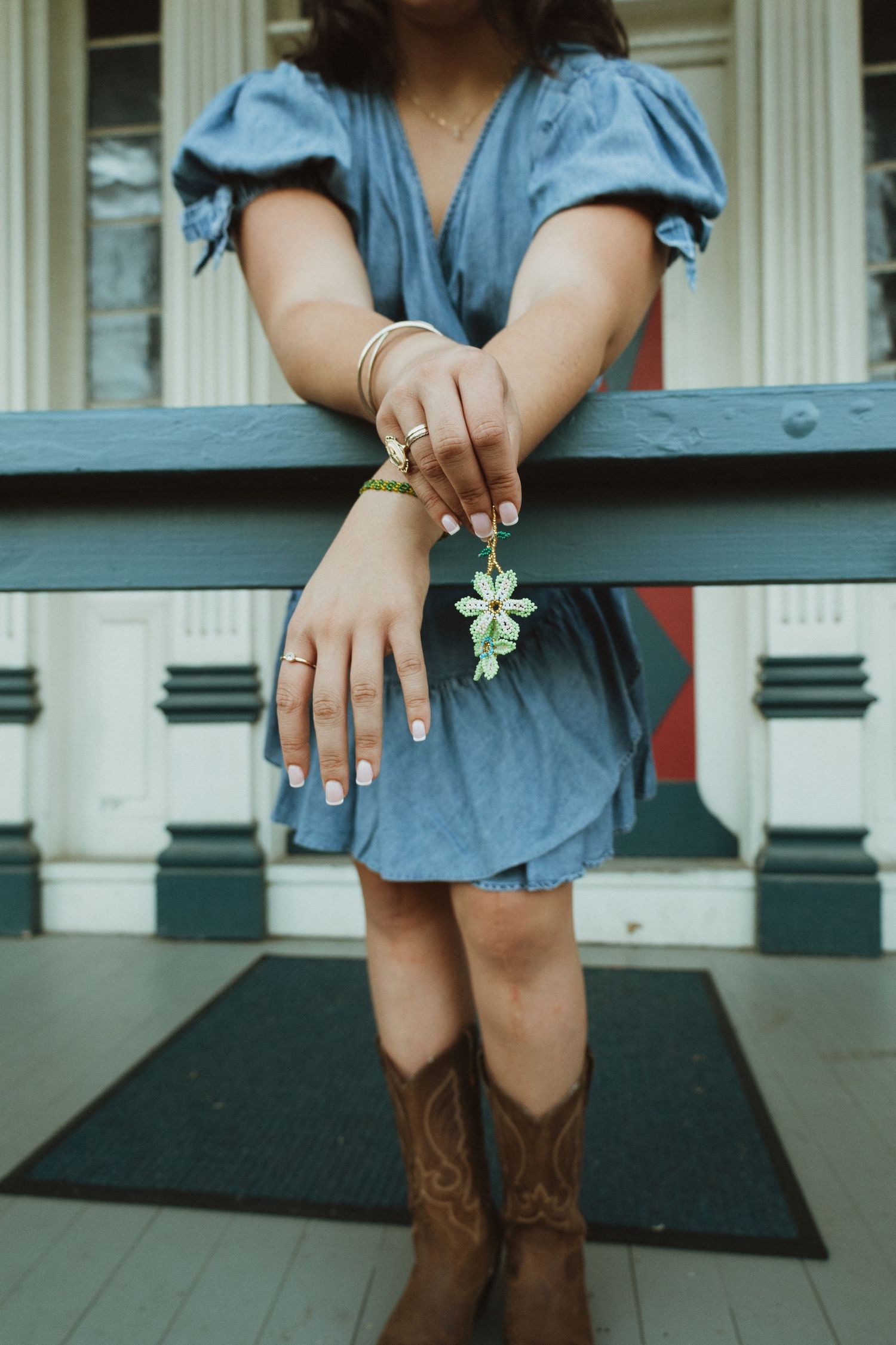 Close-up view of brown cowboy boots and hands resting on a porch railing with a blue dress visible.