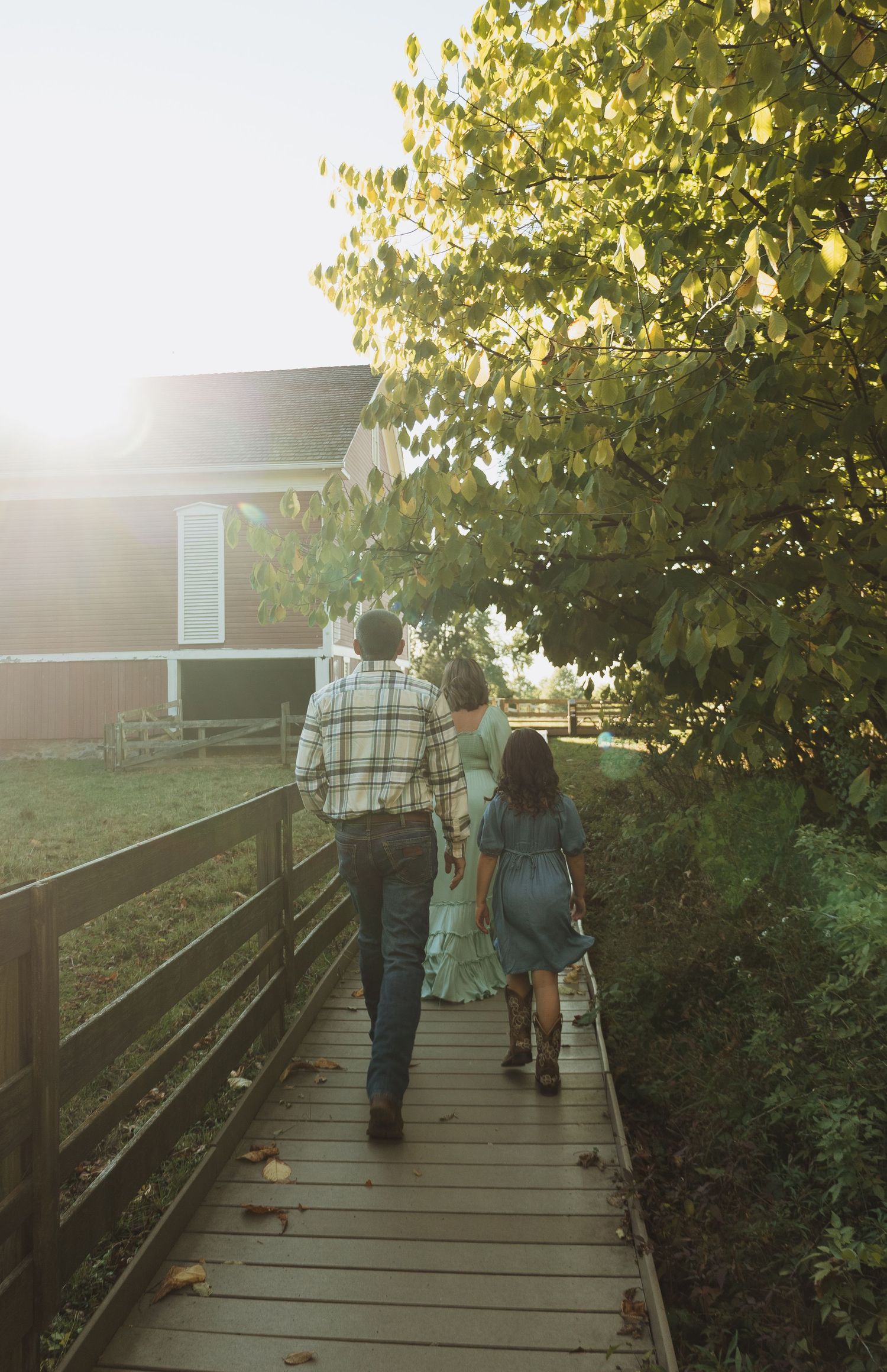 People walking on a wooden boardwalk path through autumn trees during golden hour sunlight.