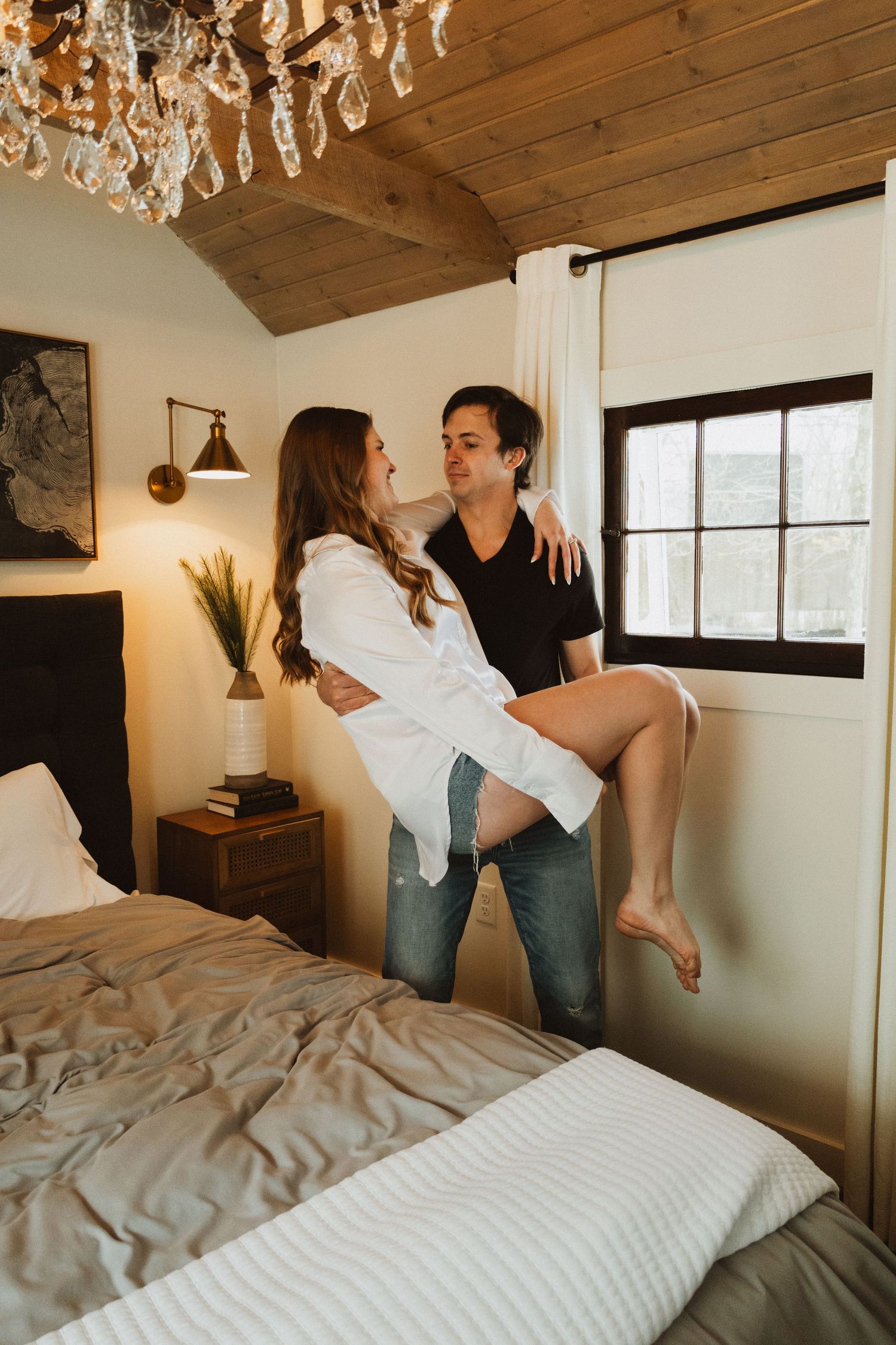 Playful moment in rustic bedroom with wooden ceiling and crystal chandelier.
