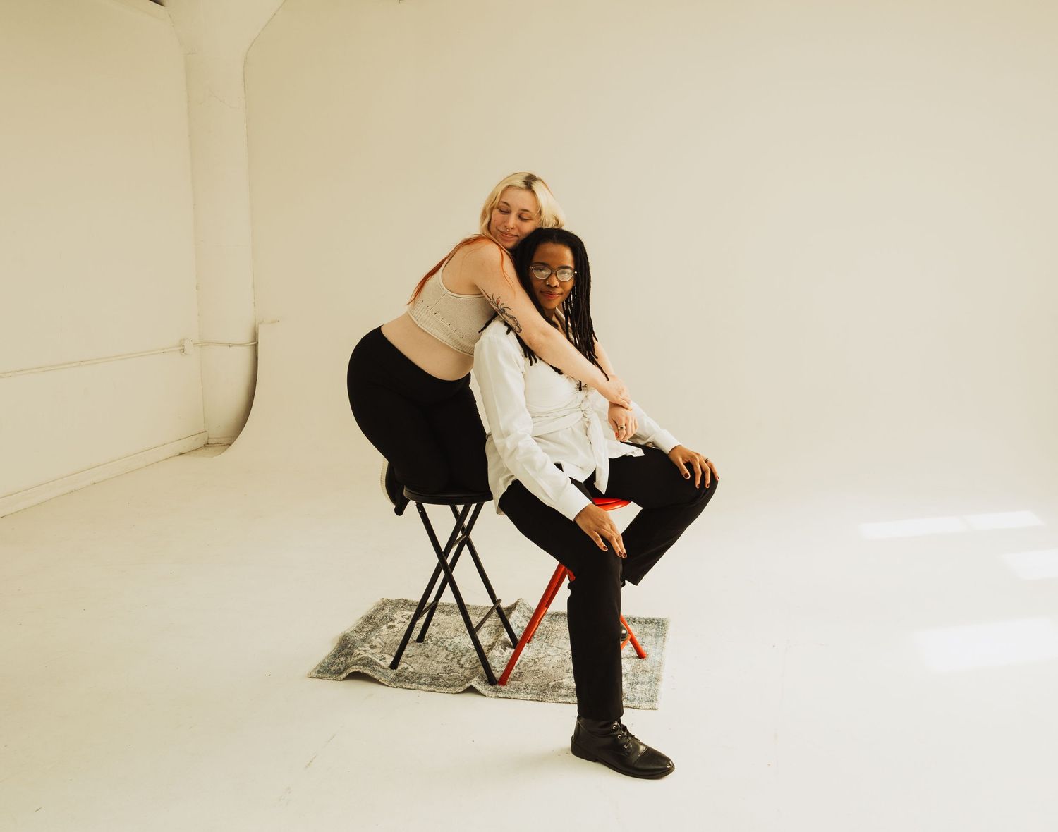 Creative duo pose on black stool in minimalist white studio setting.