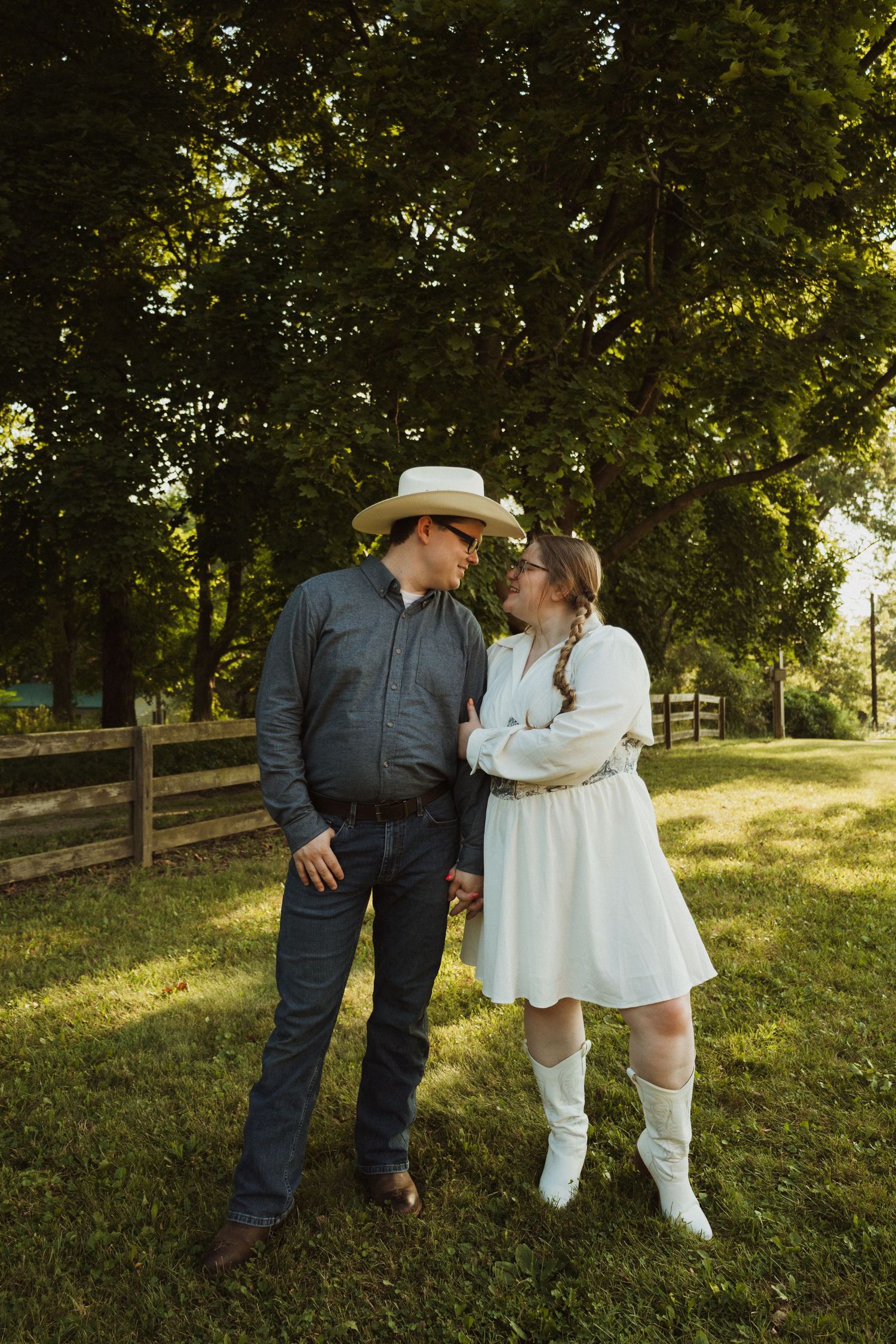 A romantic couple in western attire shares tender moments while standing in a sunlit grassy field.