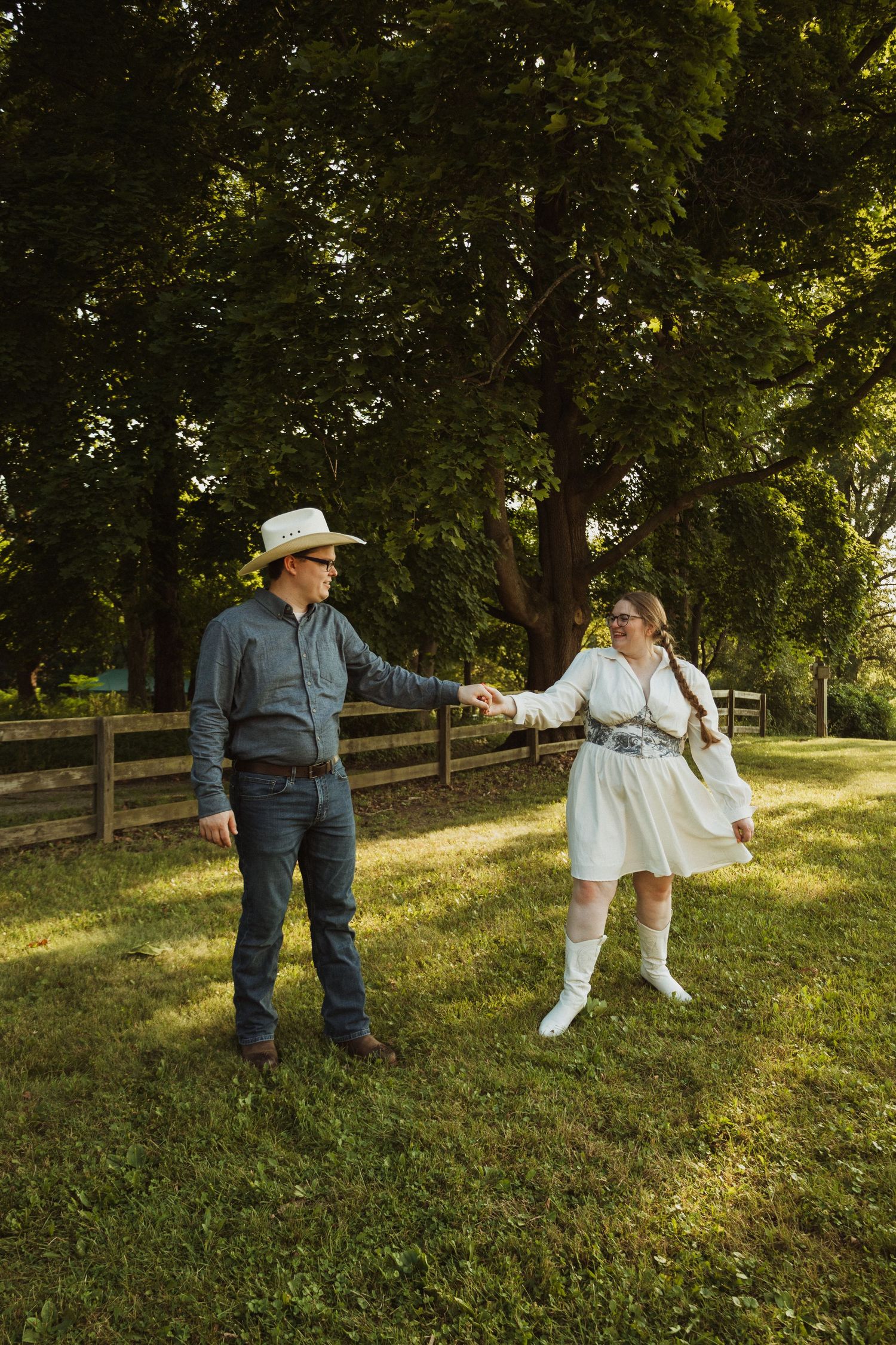 A playful dance scene unfolds on a grassy hillside with trees and wooden fence in background.