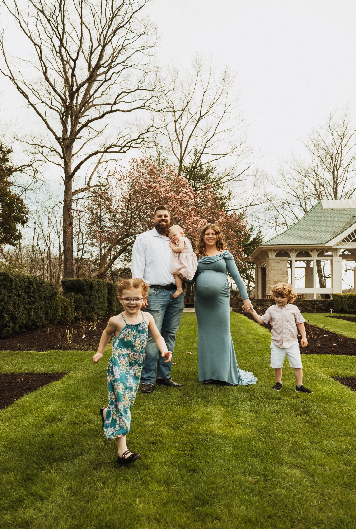 Spring family photo session in a garden with blooming trees and a vintage gazebo.