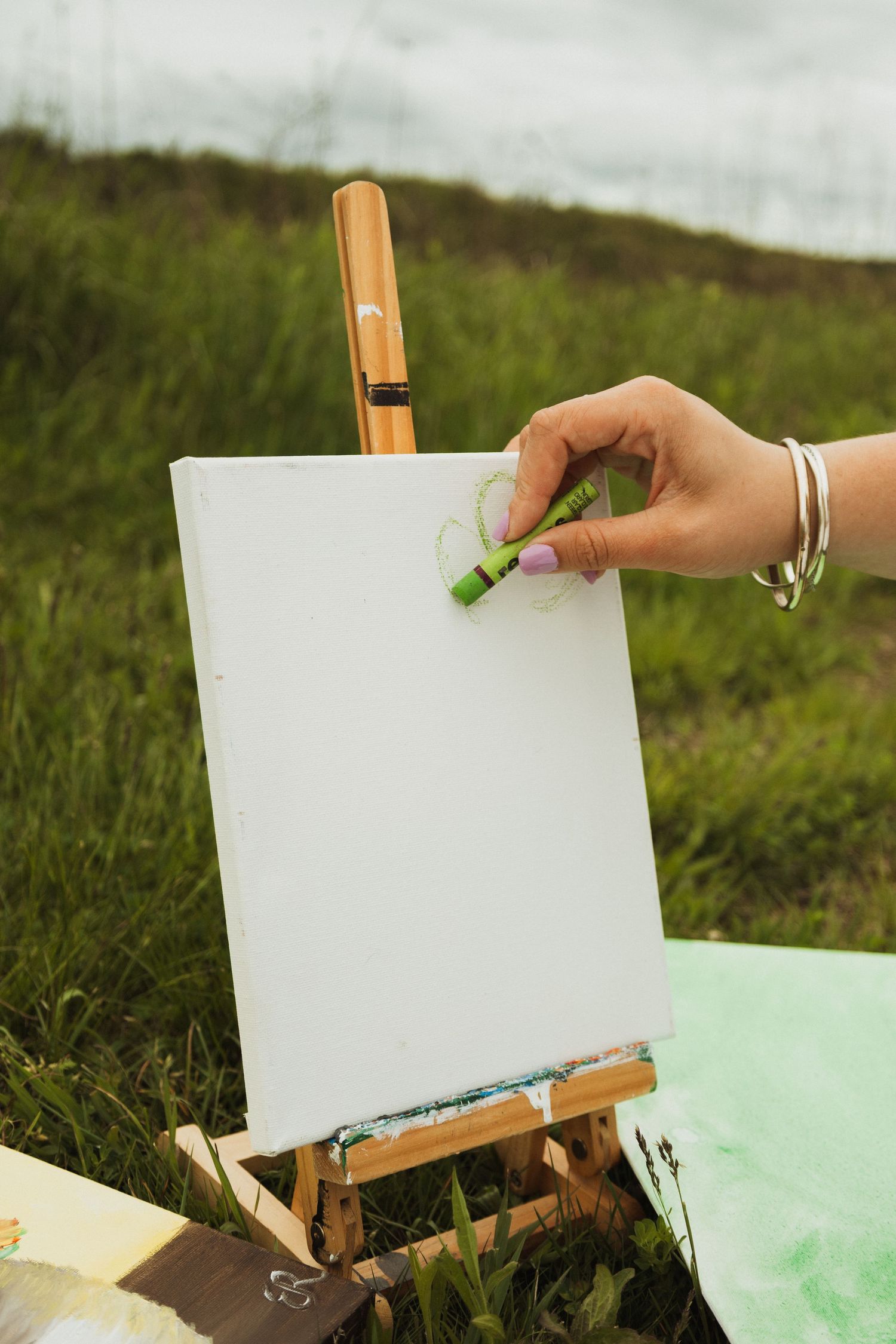 An empty white canvas rests on a wooden easel outdoors in a grassy field.