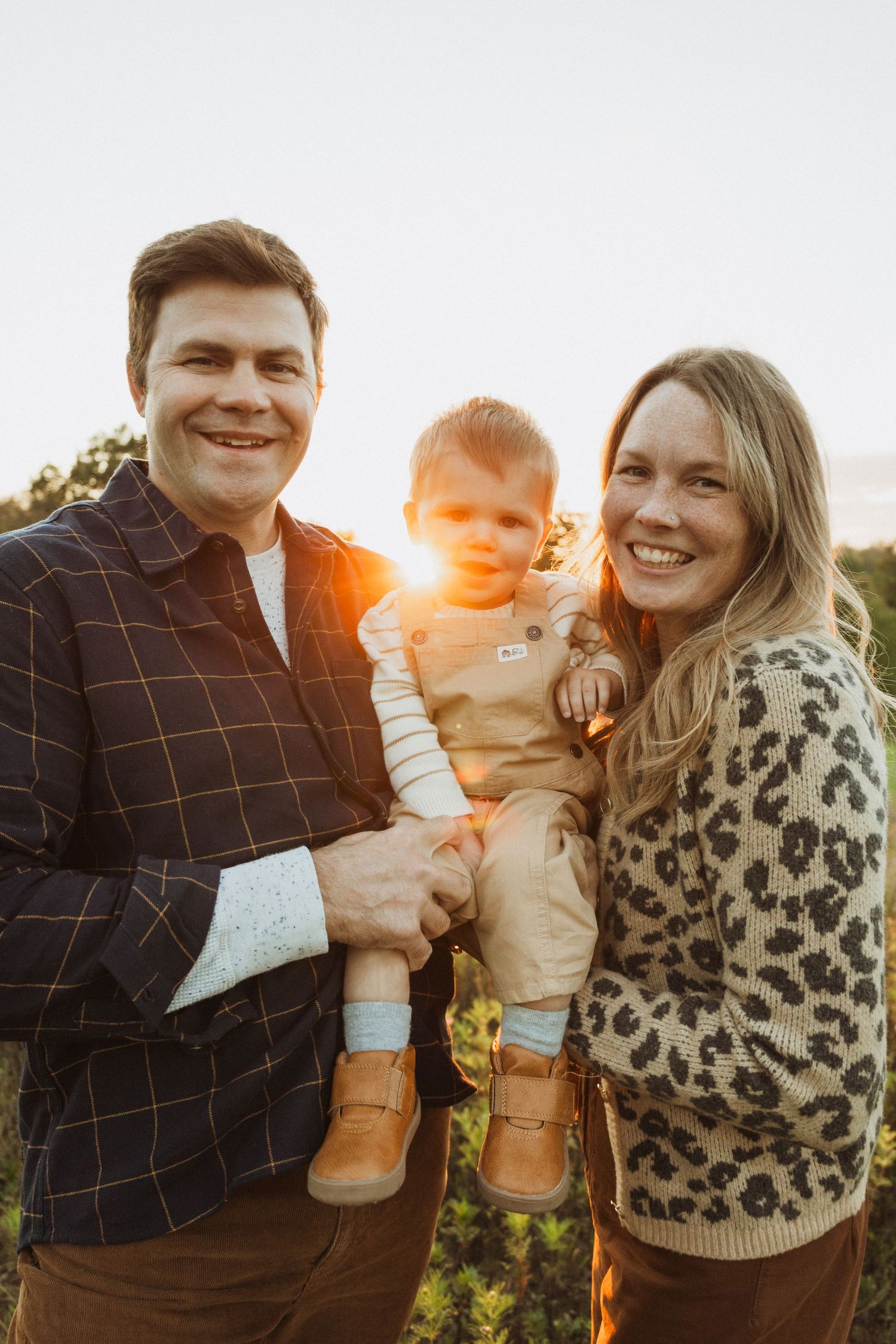 Family of three poses together during golden hour outdoors.