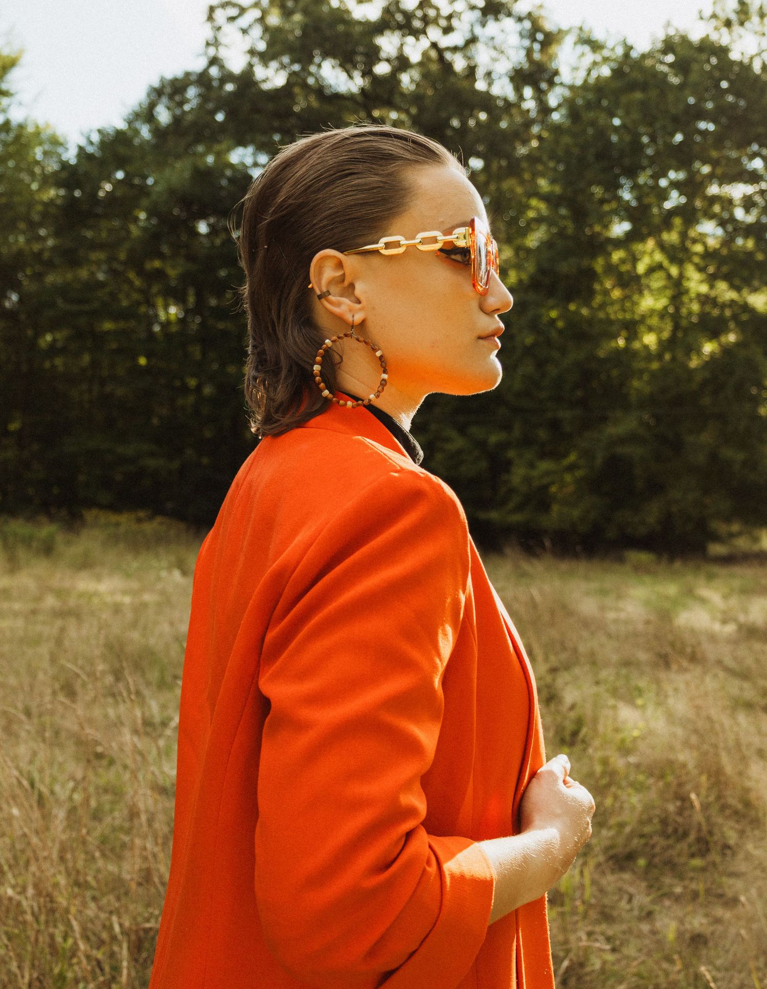 Stylish profile shot featuring bright orange blazer and retro chain-link sunglasses.