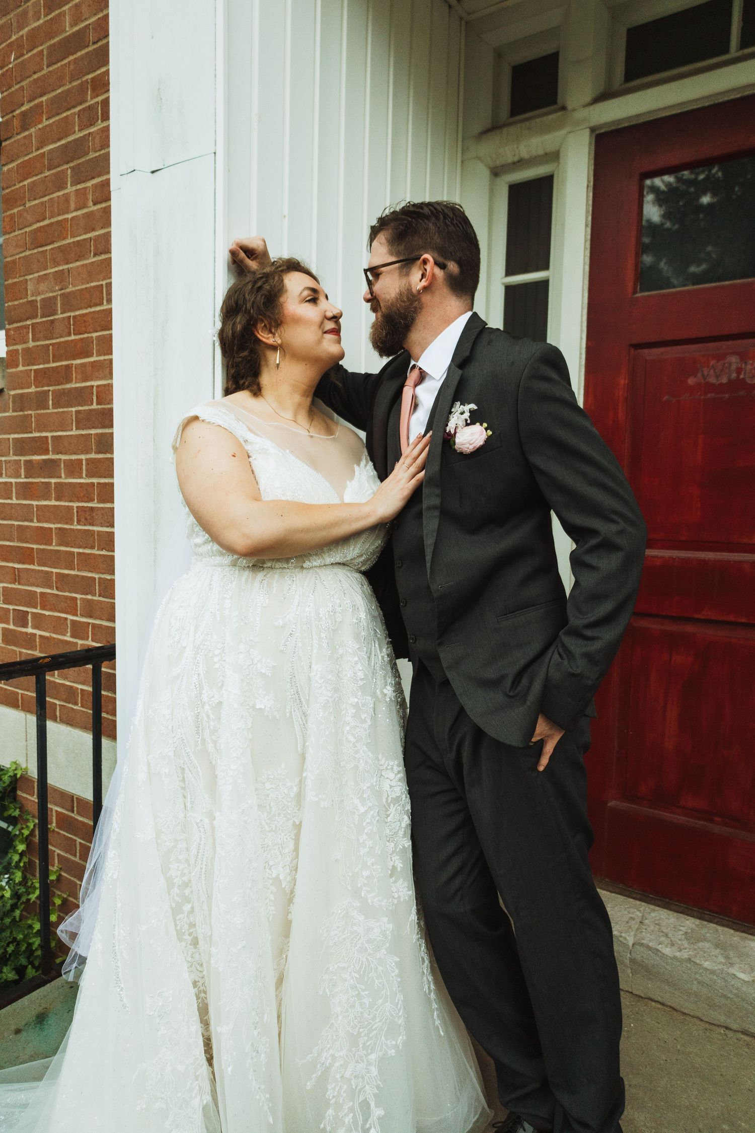 Romantic wedding couple shares intimate moments outside a brick church with red doors.