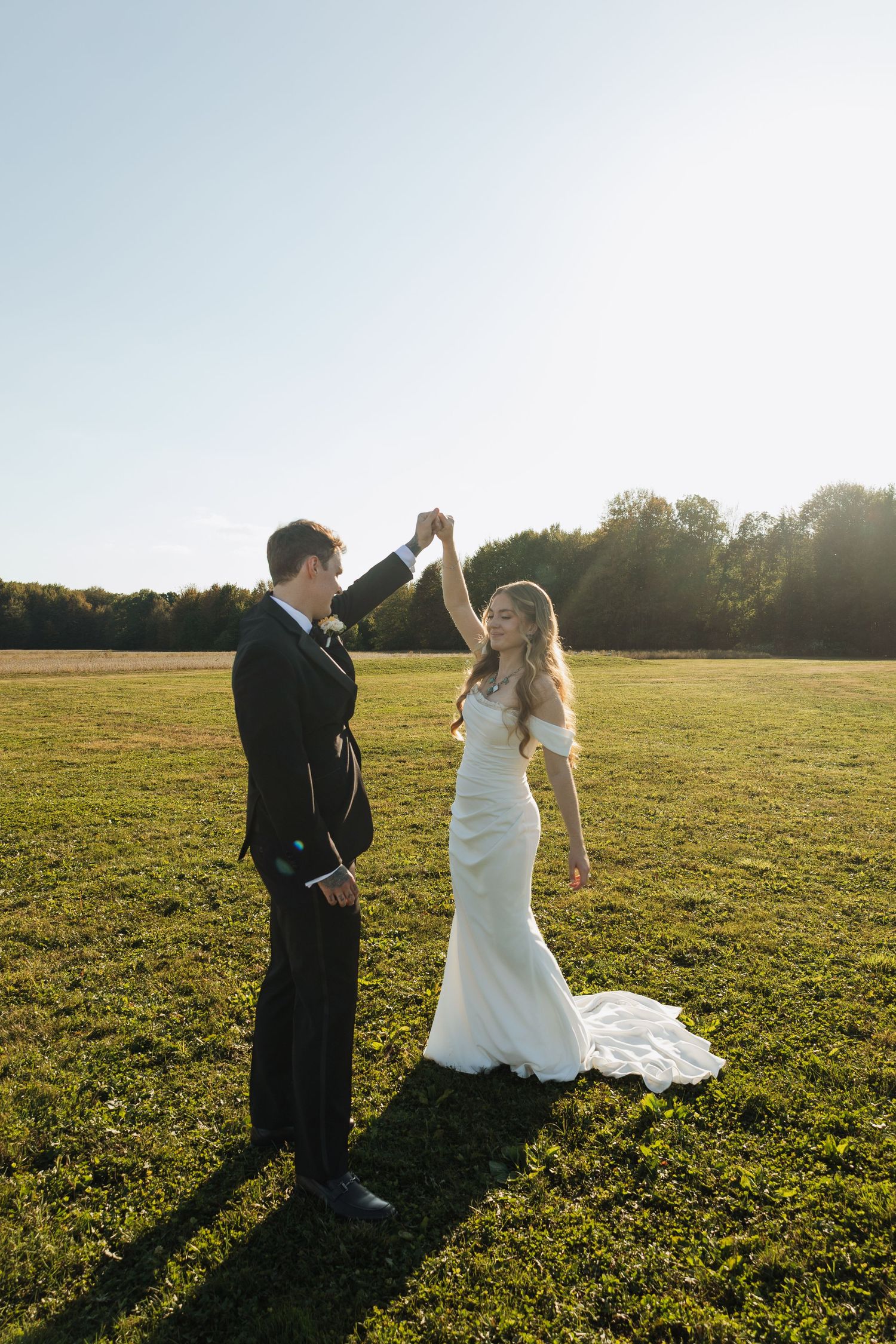 Wedding couple dancing in a sunlit meadow during golden hour.