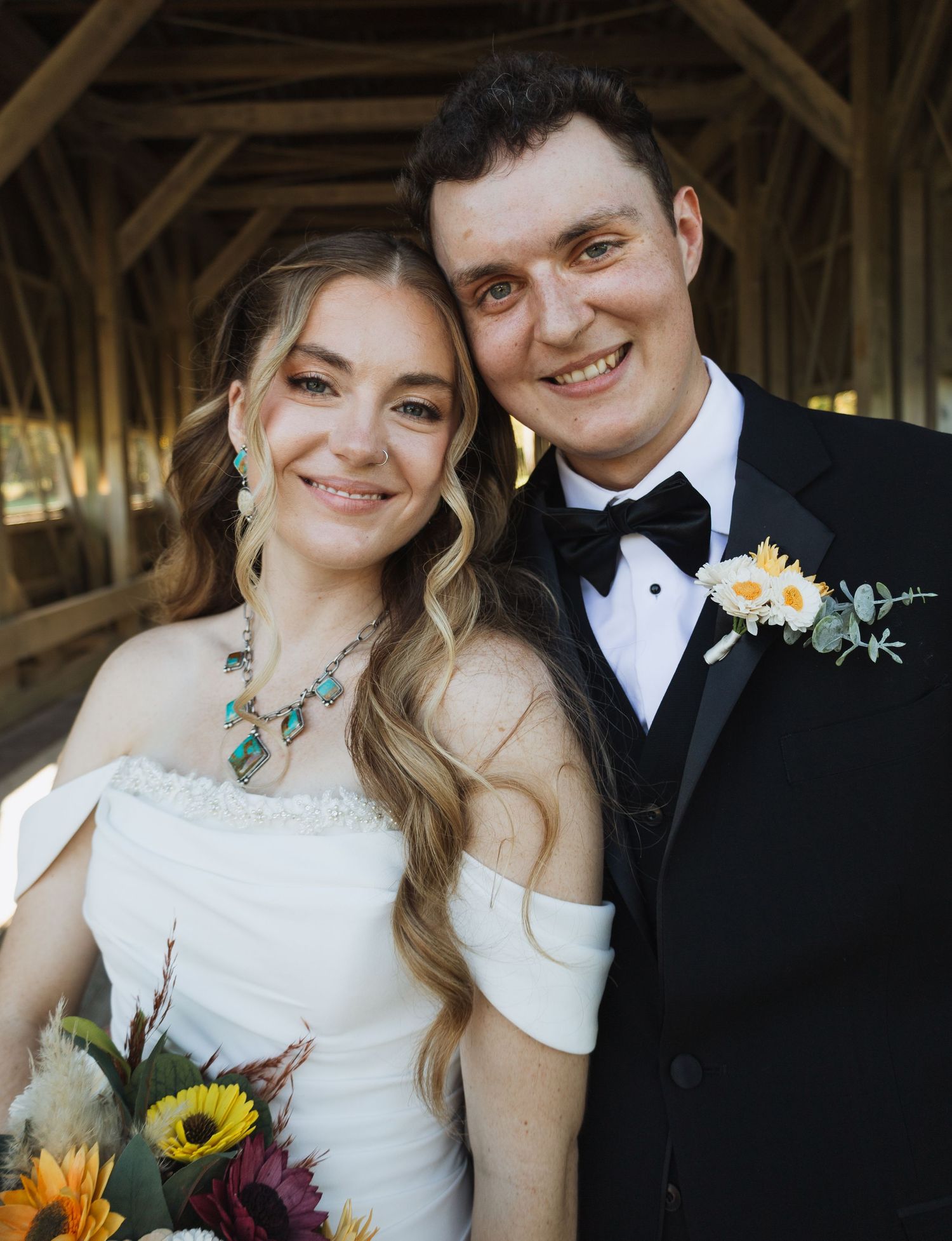 Newlyweds in formal wedding attire pose together under wooden beams.