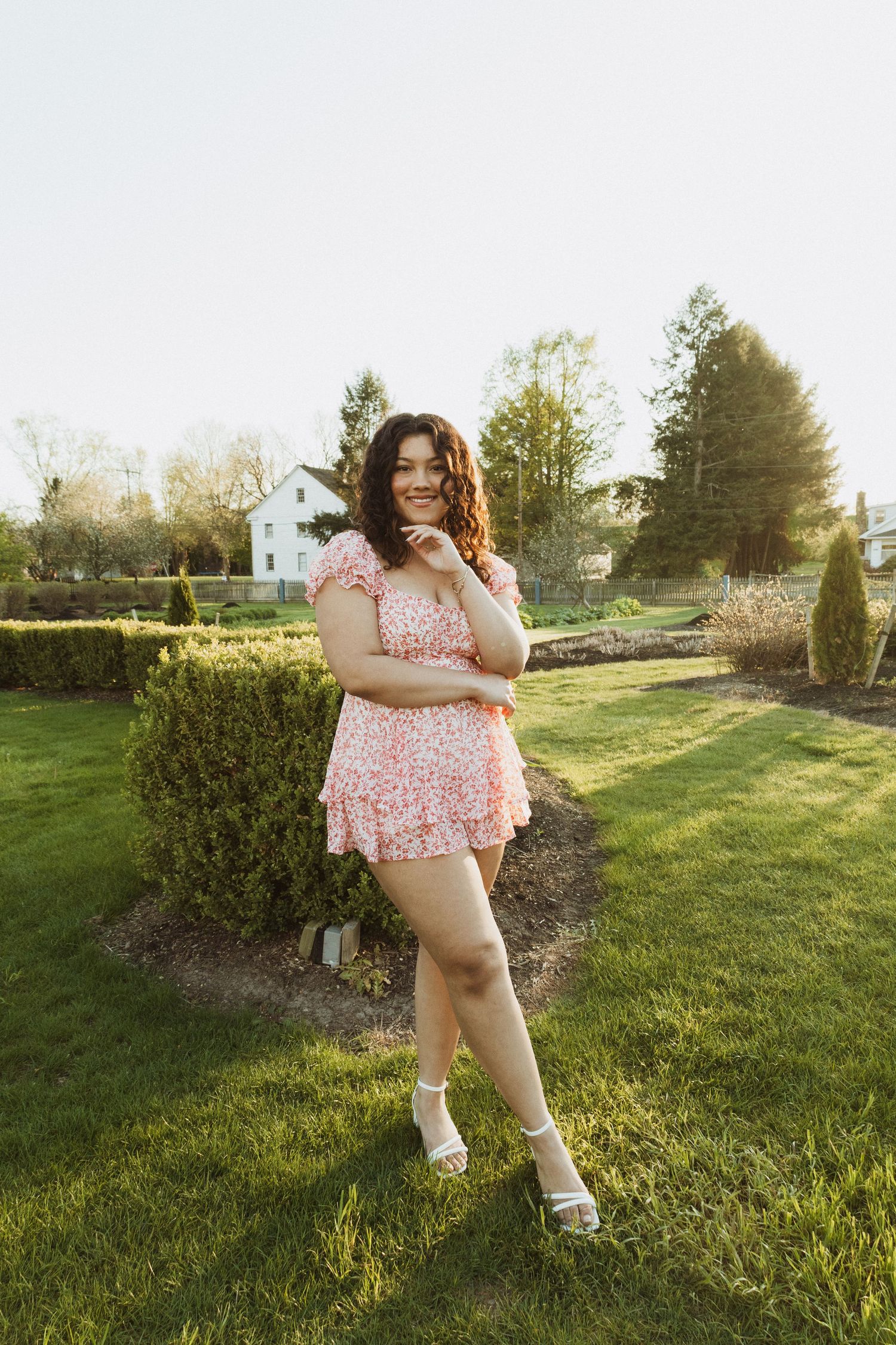 A spring fashion portrait featuring a pink floral dress in a sunny backyard garden setting.