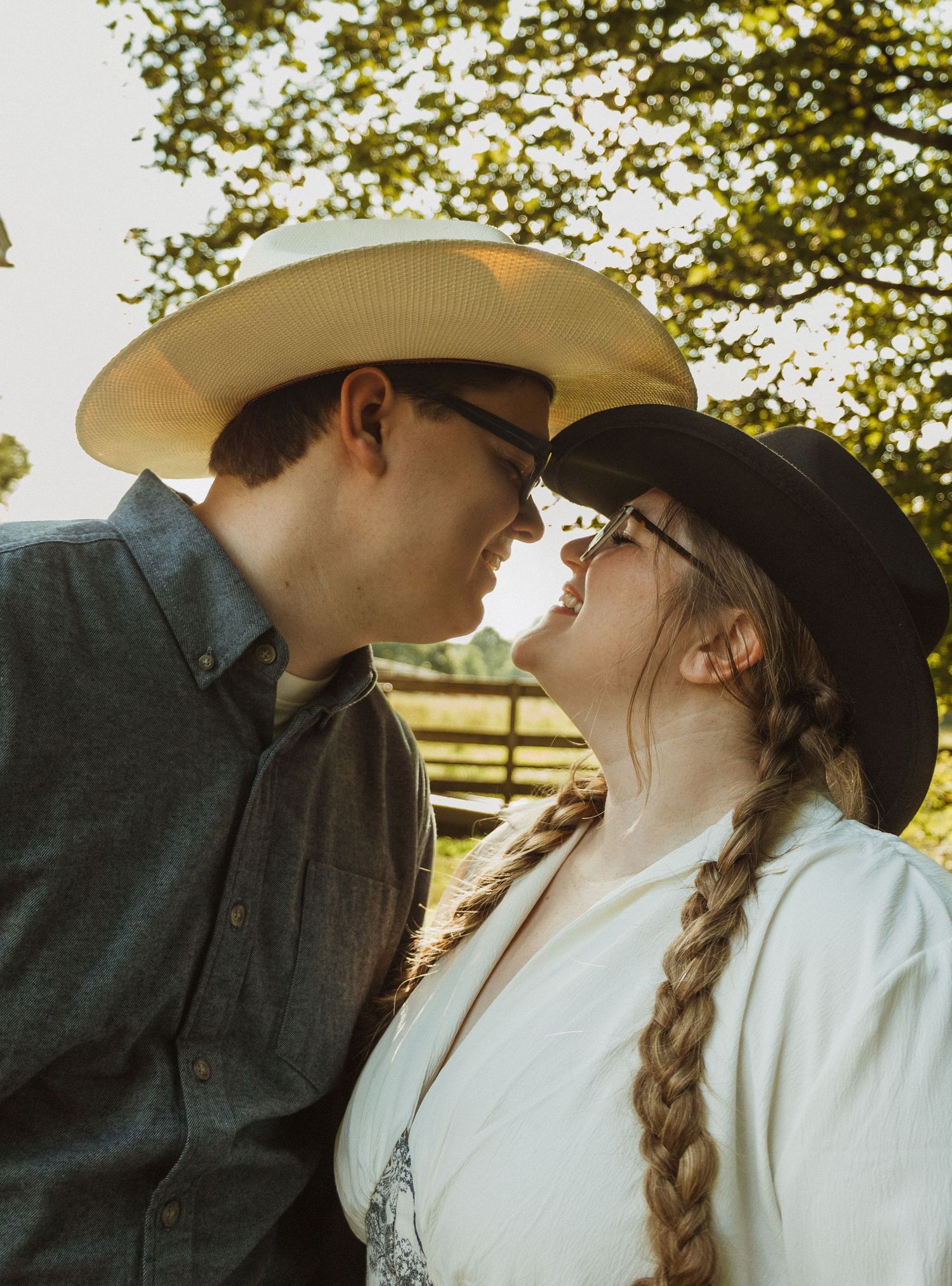 Couple in western attire sharing tender moments under sunlit trees in a romantic outdoor photoshoot series.