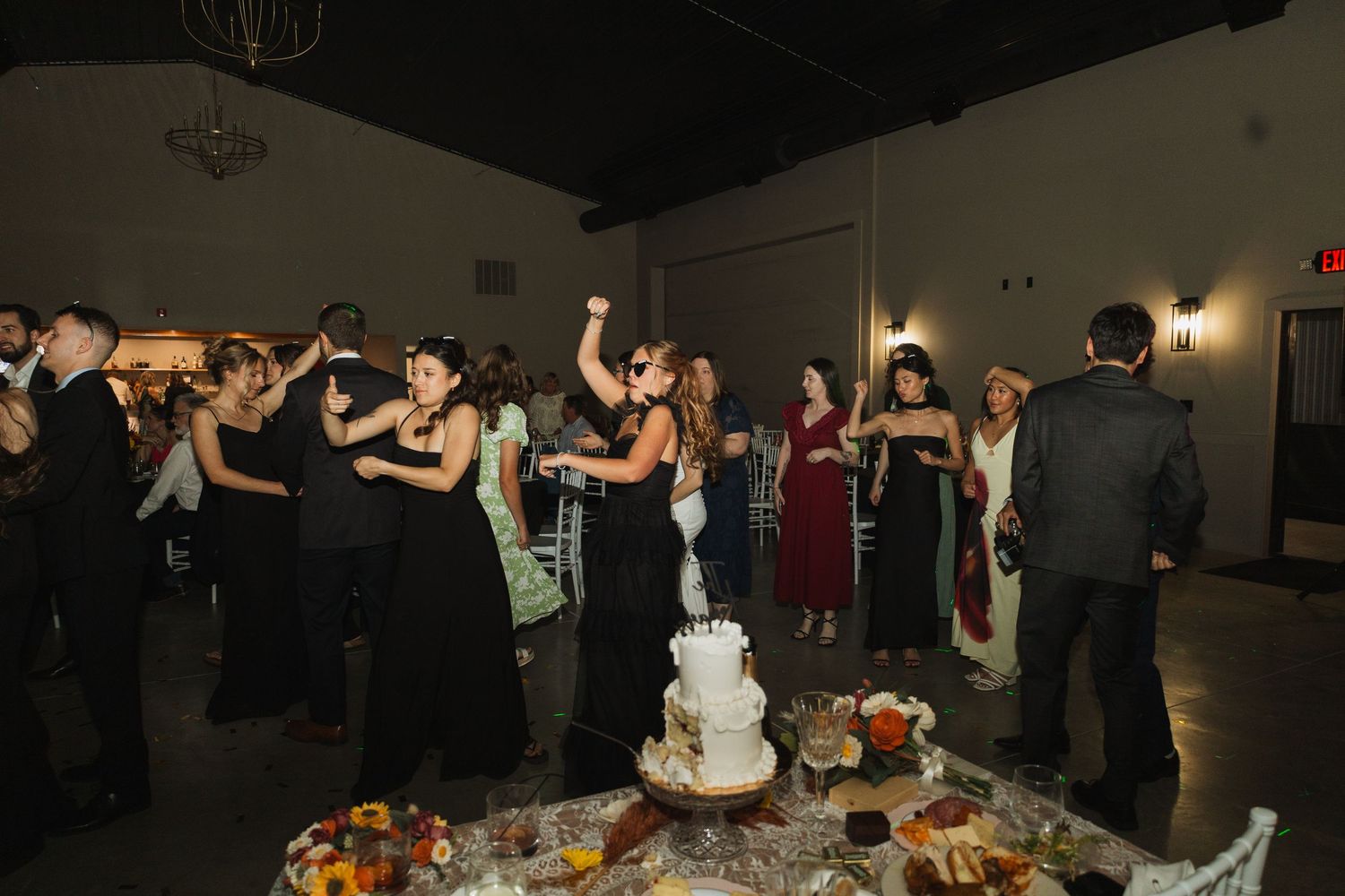 Wedding reception guests dancing and celebrating on a dark dance floor with festive lighting.