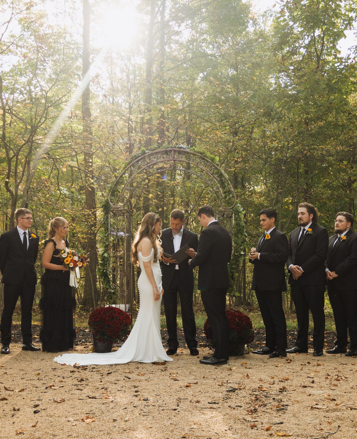 Outdoor wedding ceremony in a wooded area with autumn leaves on the ground.