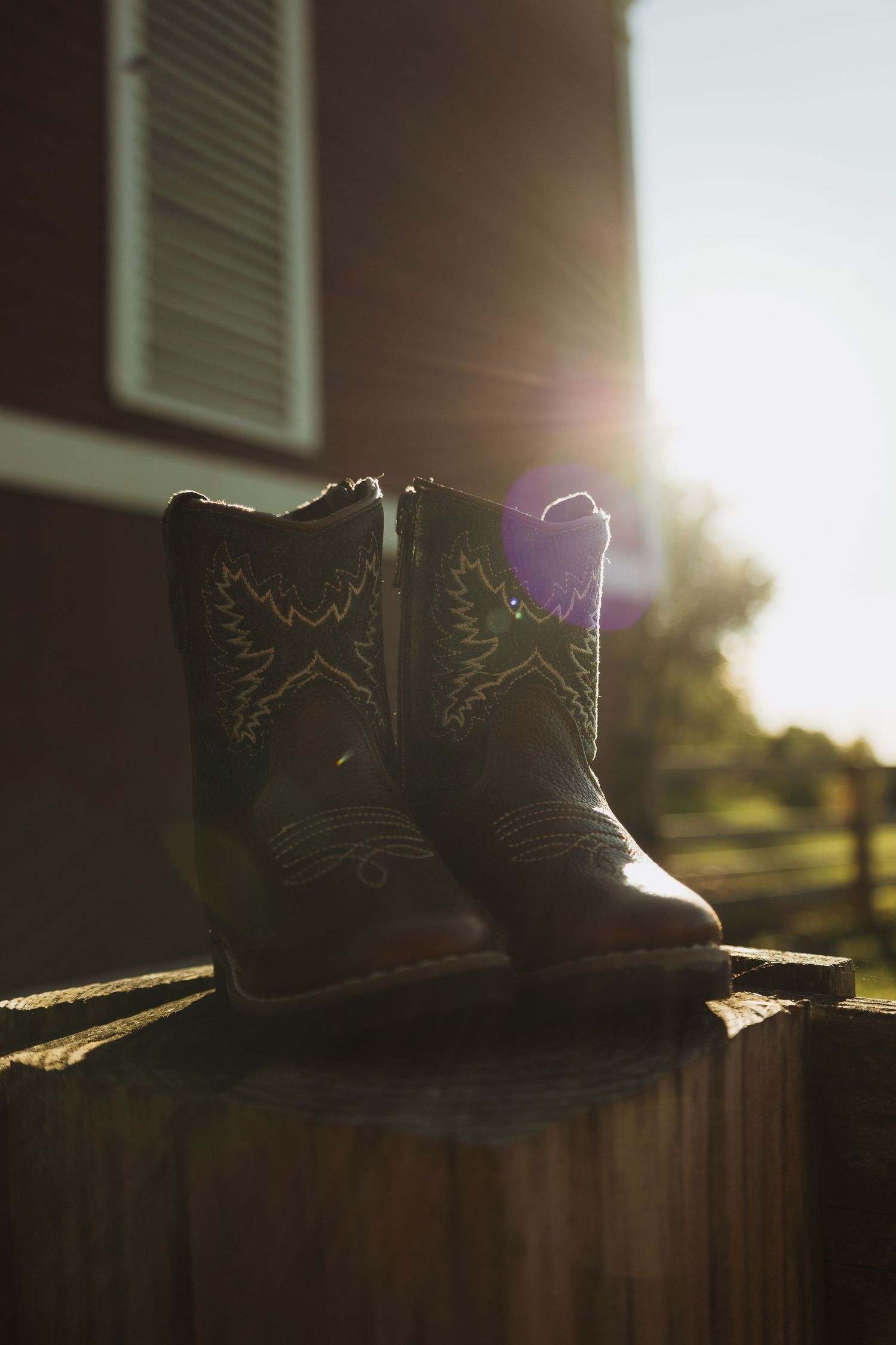 A pair of cowboy boots sits on a wooden surface in dramatic sunlight with lens flare effects.