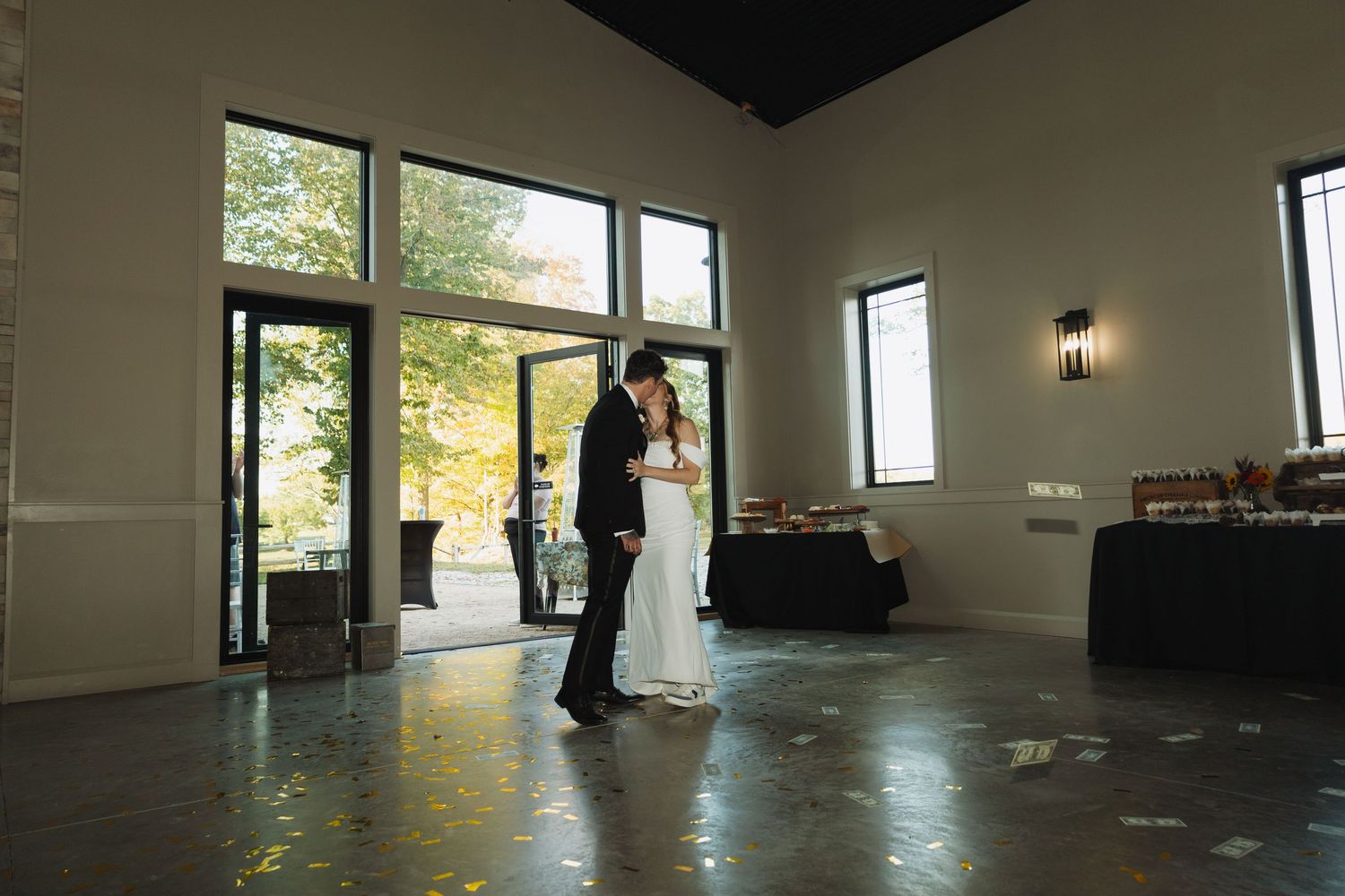 A couple shares their first dance in a modern venue with floor-to-ceiling windows and natural light.