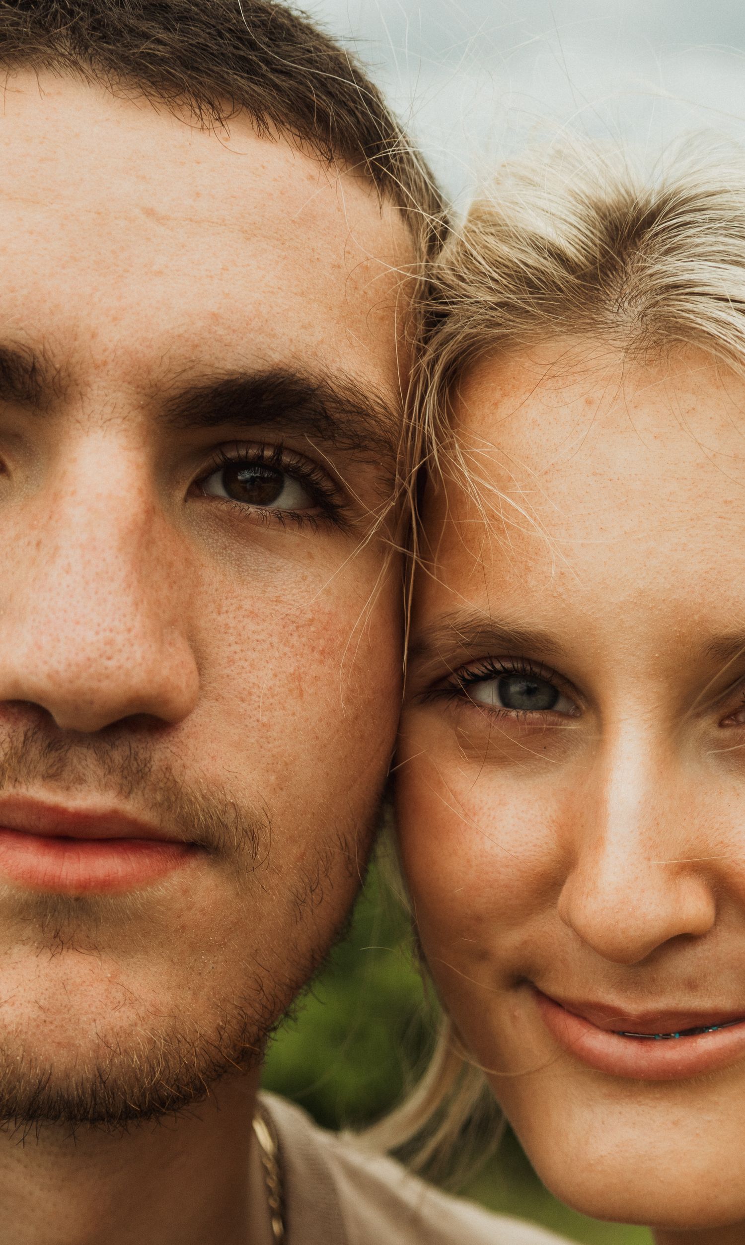 An intimate close-up portrait of a couple against a natural outdoor background.