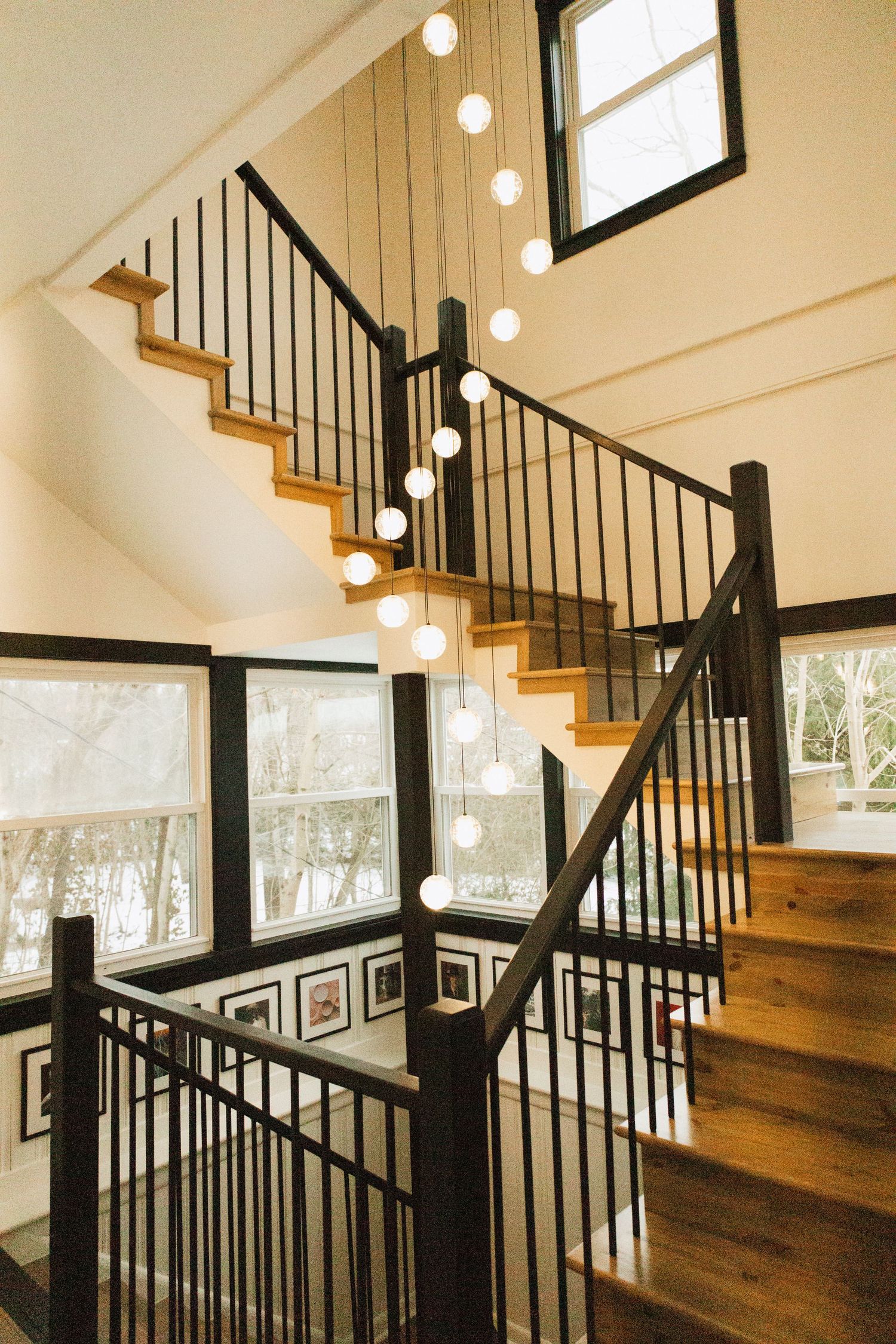 Modern staircase with wooden steps and black railings illuminated by hanging pendant lights.