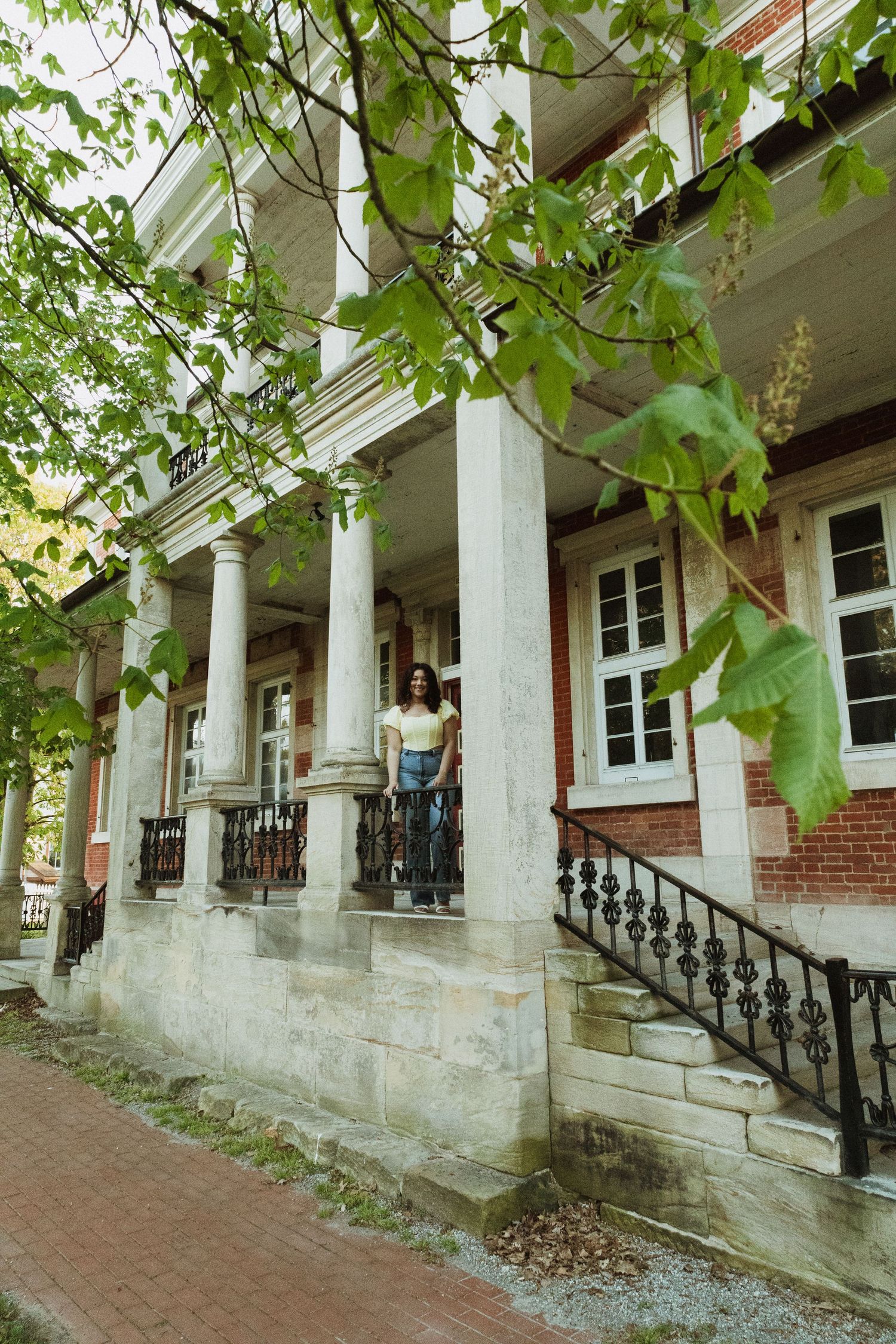 Historic building exterior with white columns and brick walls framed by green leaves.