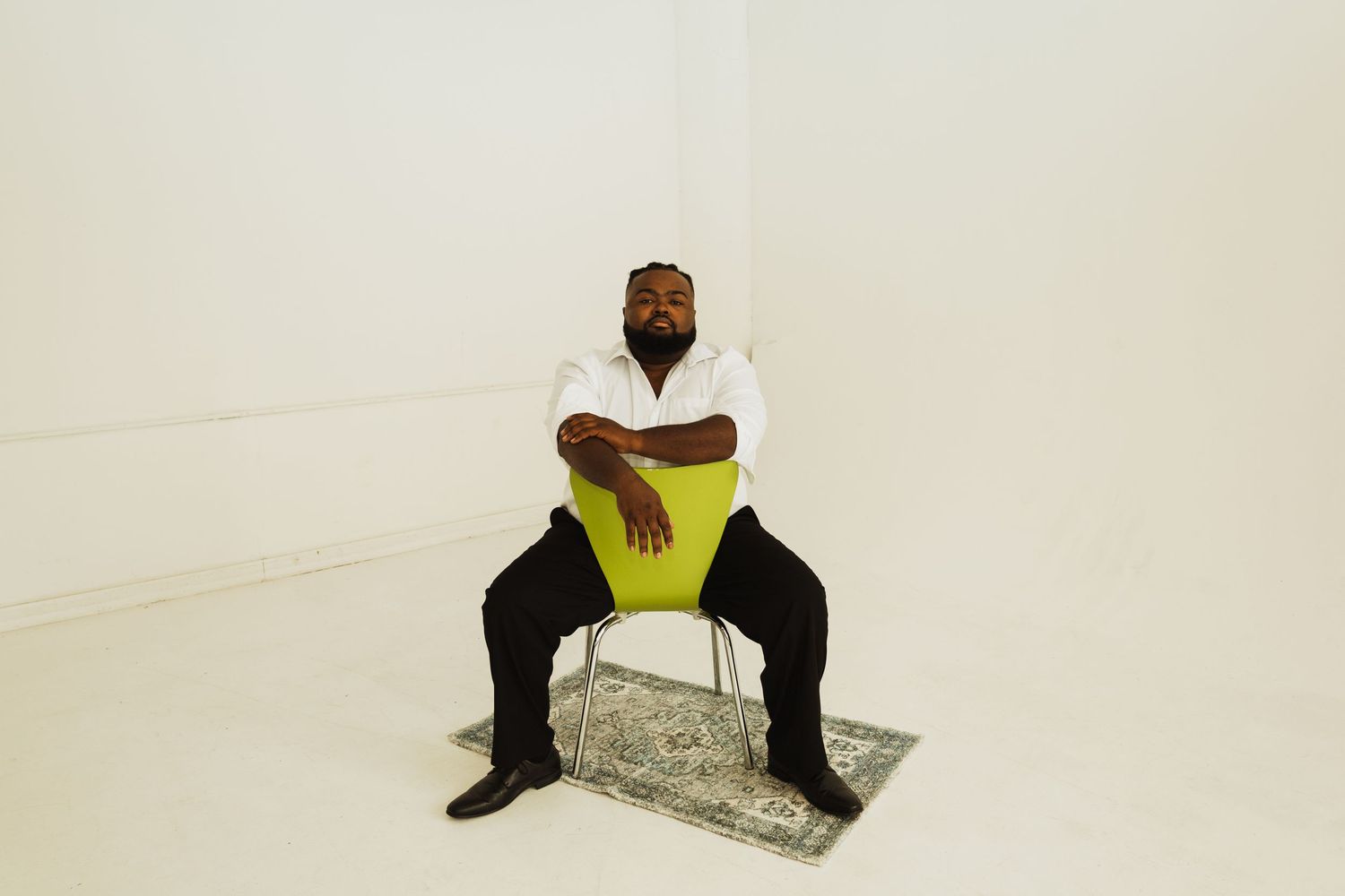 A person sits in a modern green chair against a white backdrop in a minimalist studio setting.