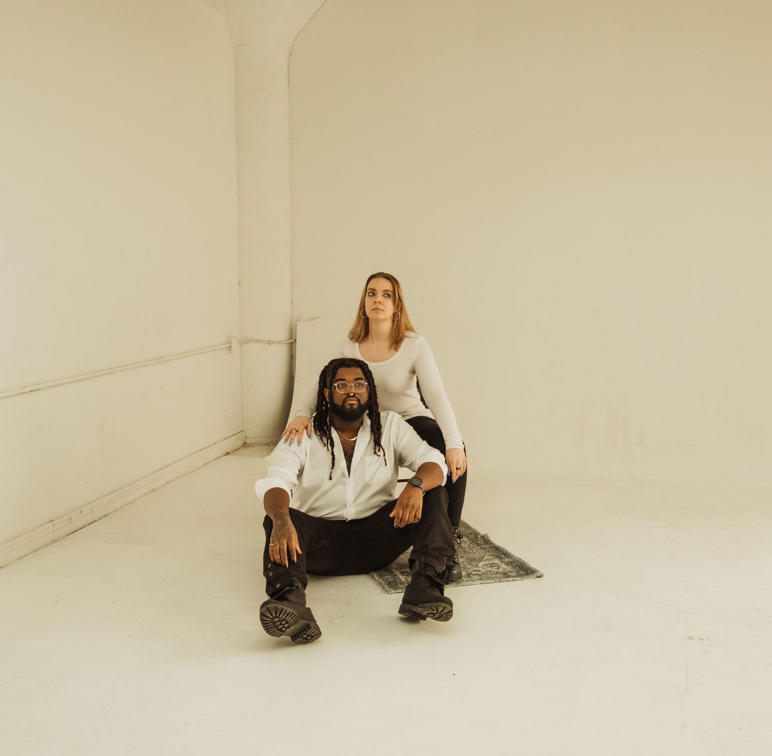 Artistic portrait with two people in casual wear posed in bright studio space.