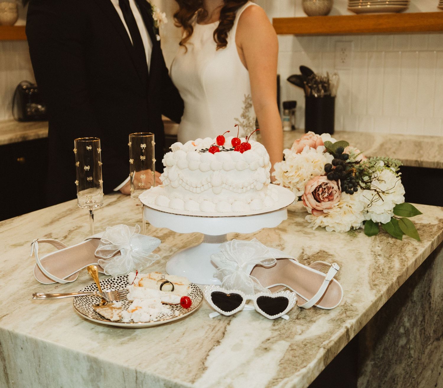 Wedding details including heart sunglasses and cake on marble countertop with floral decorations.