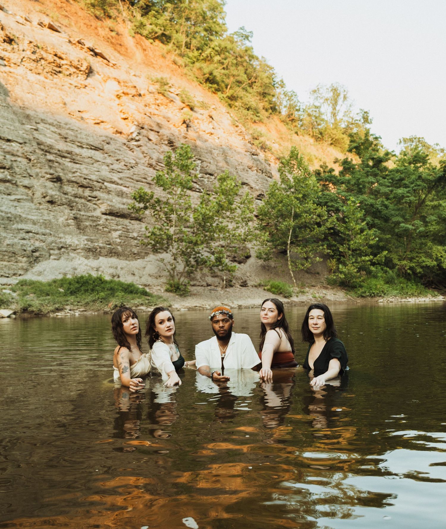 Group enjoying a summer day while wading in clear water beneath towering limestone cliffs.