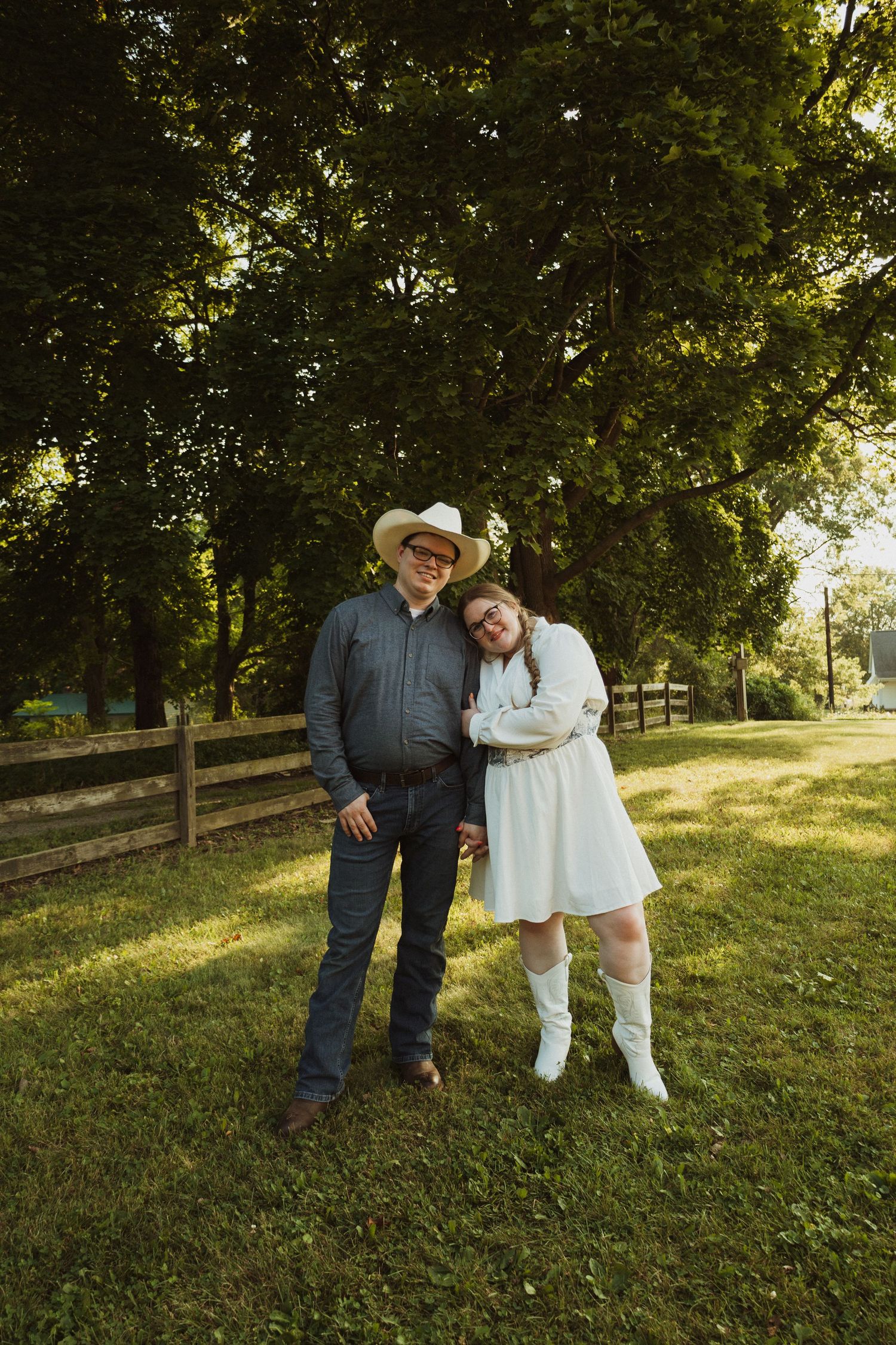 A couple shares a tender moment in a beautiful outdoor setting with green grass and trees at golden hour.