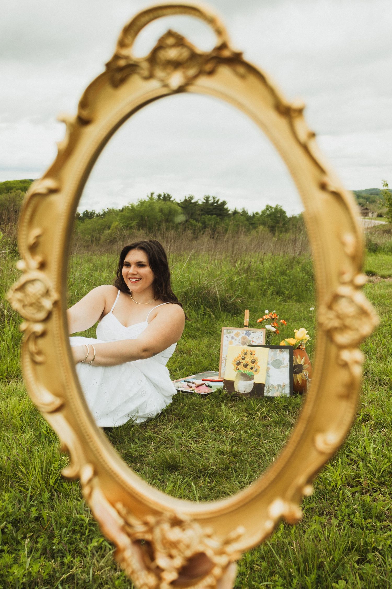 A decorative gold vintage mirror frame creates artistic compositions in a grassy outdoor meadow setting.
