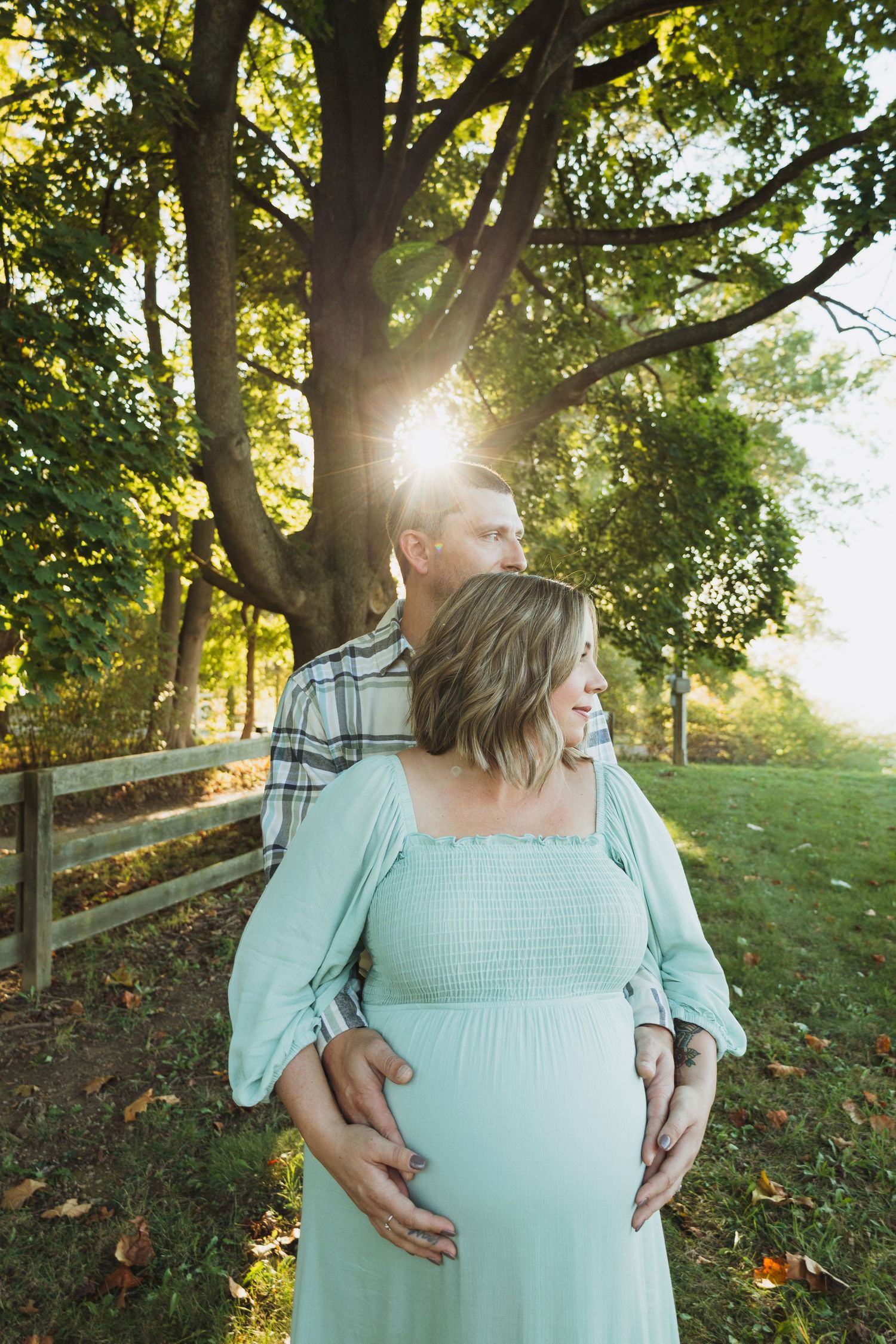 A couple embraces in a sunlit garden setting with autumn leaves and wooden fencing creating a romantic atmosphere.