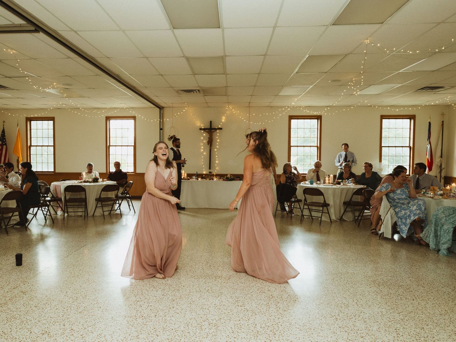 Wedding guests in formal attire dance and celebrate in a large reception hall.