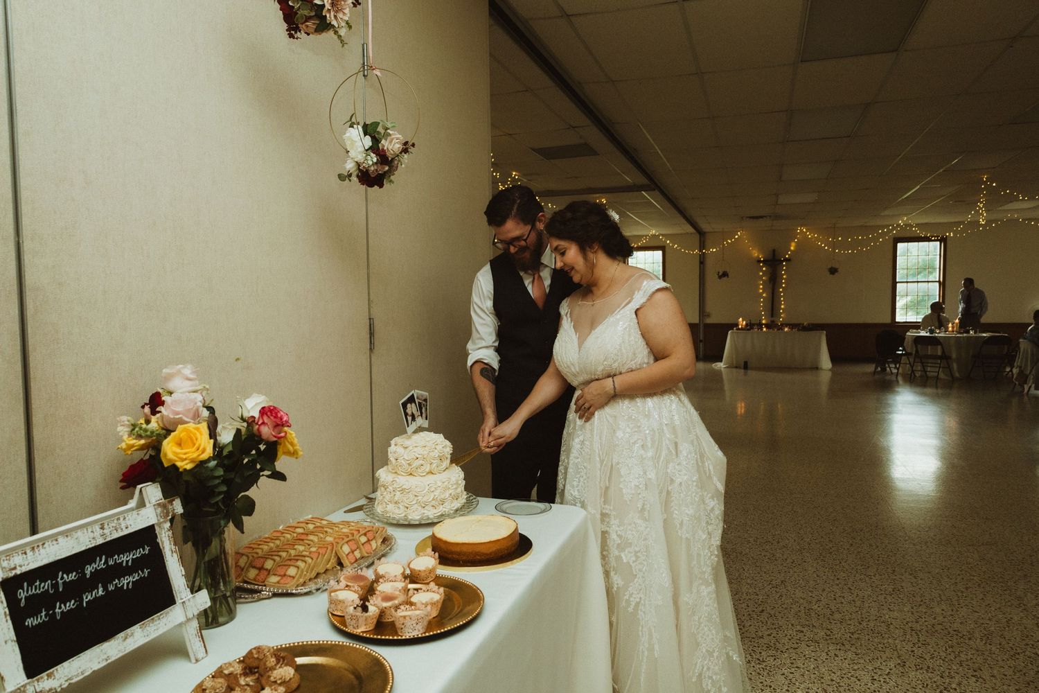 Wedding reception setup with rustic decor showing dessert table and floral arrangements in a banquet hall.