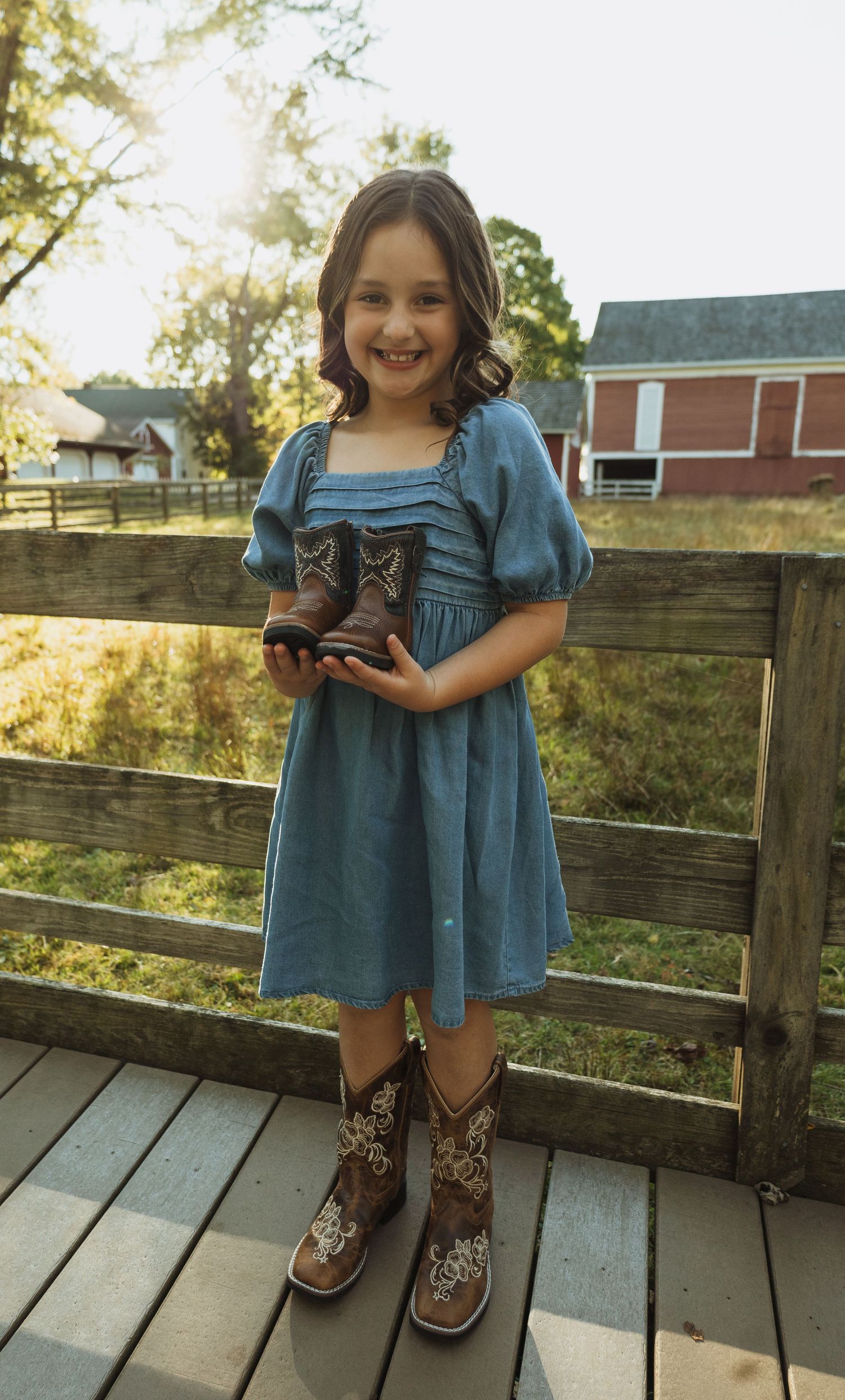 A child in a blue dress and patterned leggings stands on a wooden deck during golden hour.