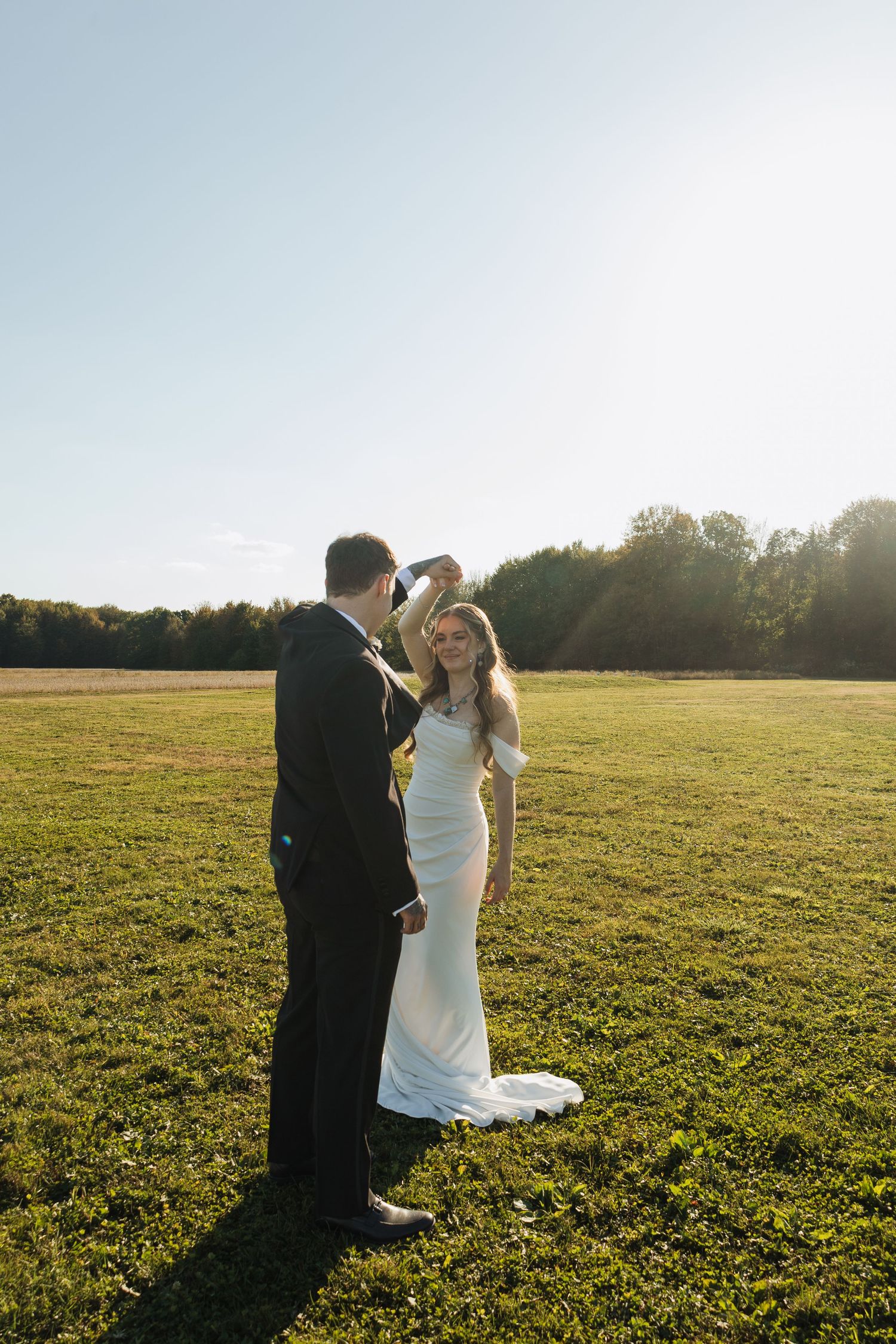 A couple shares a romantic moment in a sunlit field with autumn trees in the background.