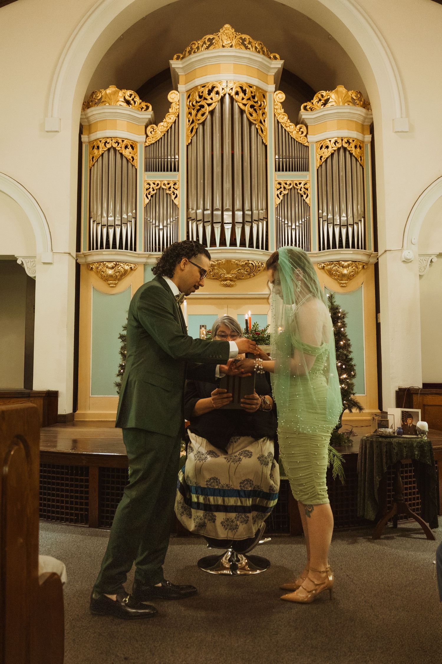 Couple exchanging vows before grand pipe organ in historic church with Christmas decor.