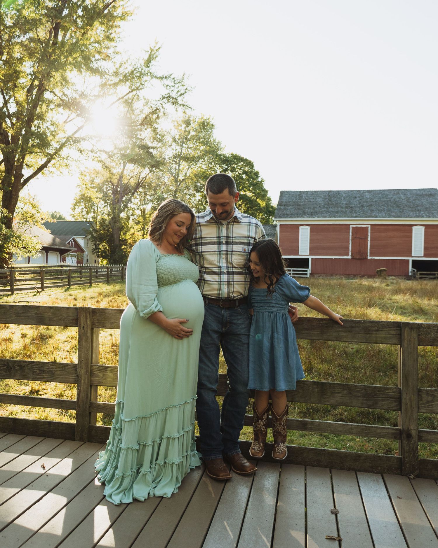 Family members stand on rustic wooden deck during golden hour with rural scenery behind them.