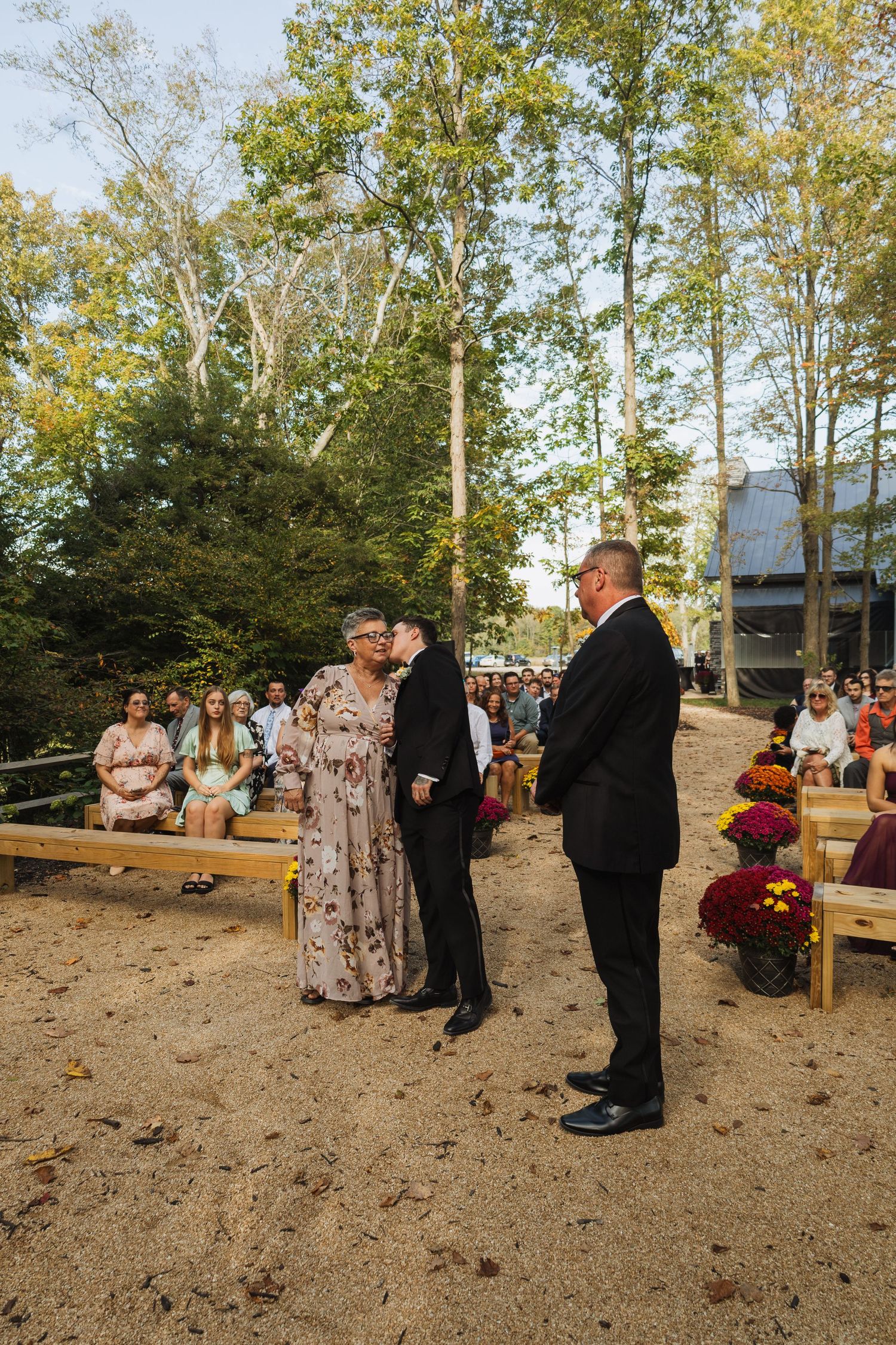 Outdoor wedding ceremony setup with wooden benches and autumn trees in a rustic woodland setting.