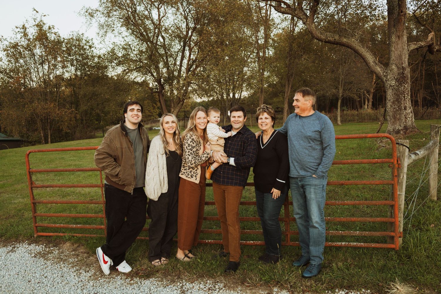 Group posed casually against metal farm gate in outdoor rural setting.