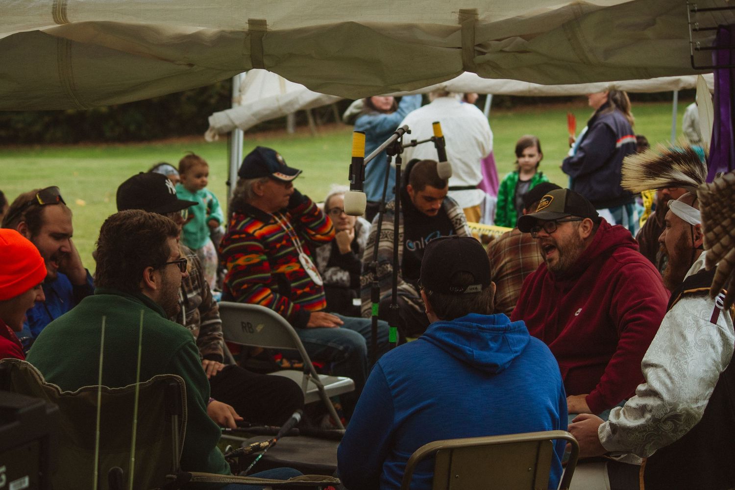 A group gathers outdoors under canopy tents at what appears to be a cultural festival or community event.